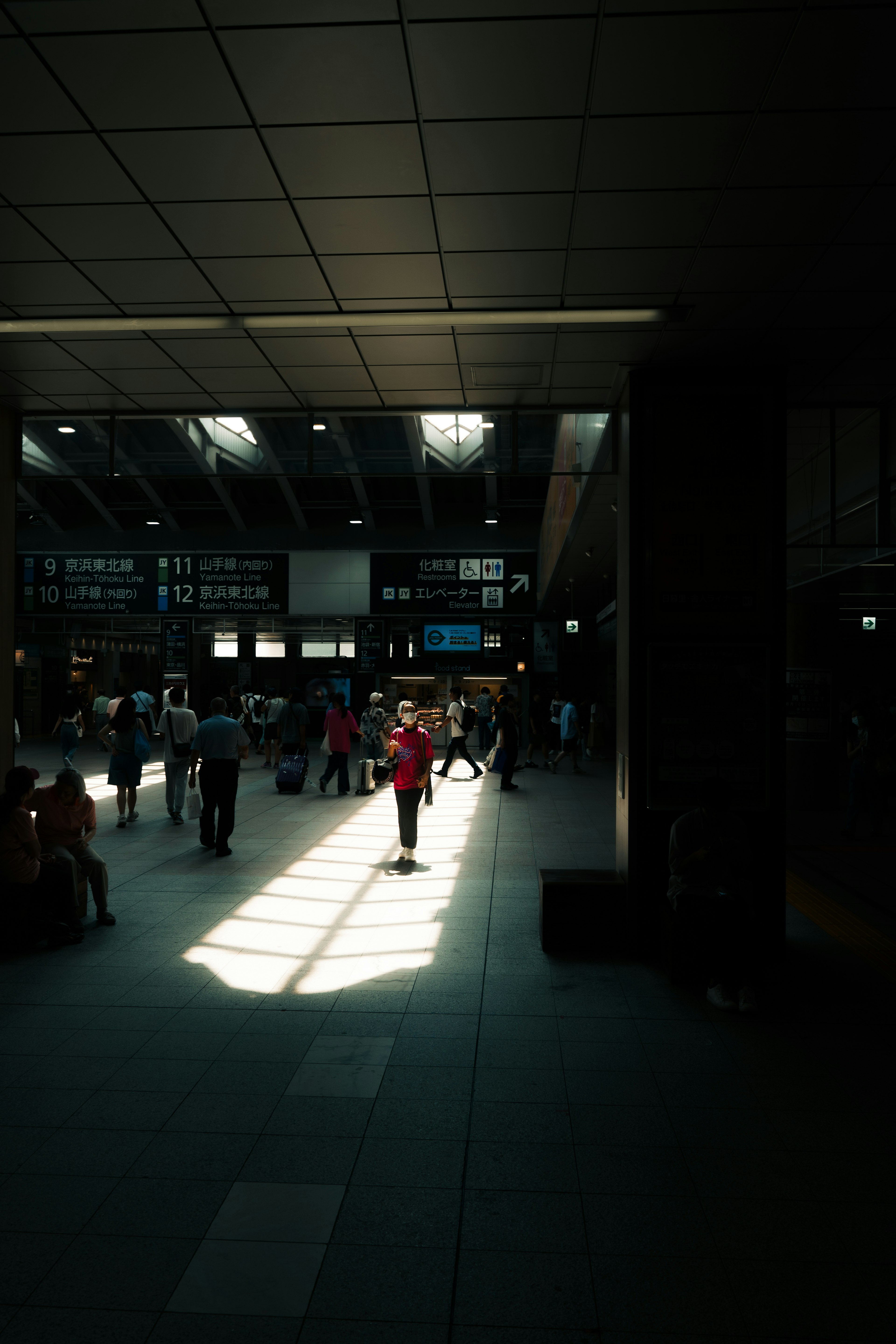 駅の内部に人々がいる明るい空間で、光の道が床に映し出されている