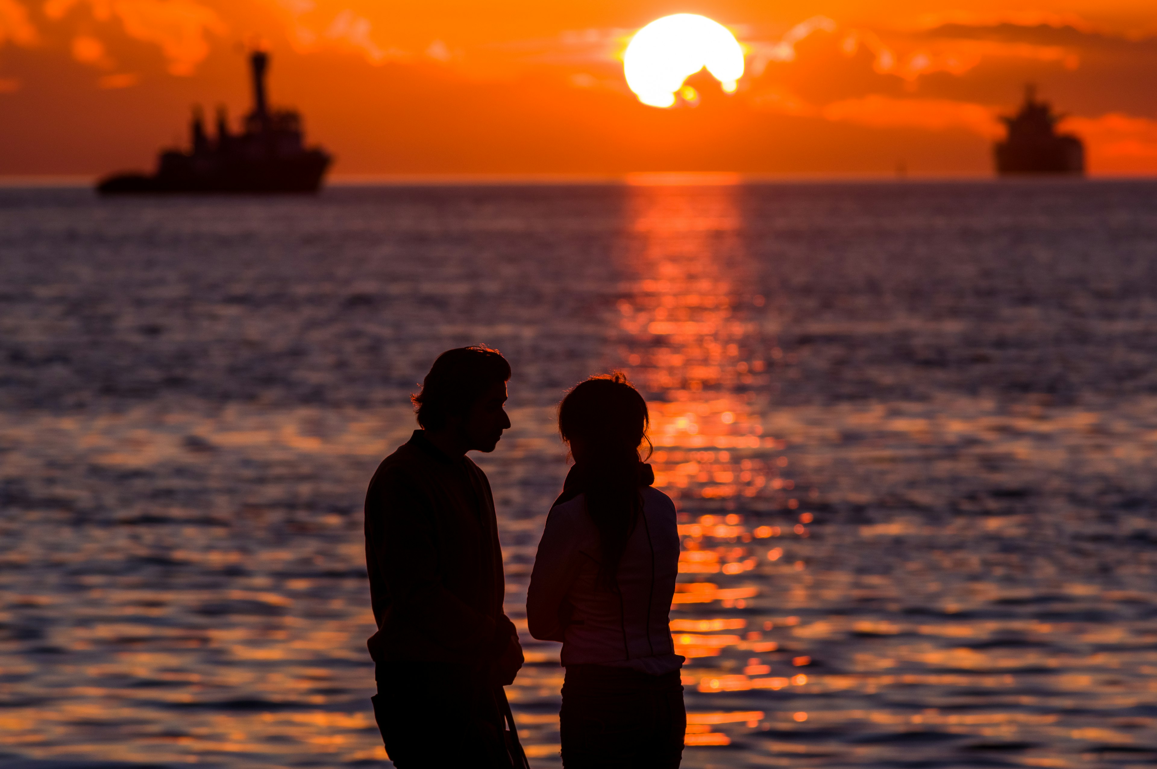 Silueta de una pareja hablando junto al mar con un atardecer de fondo