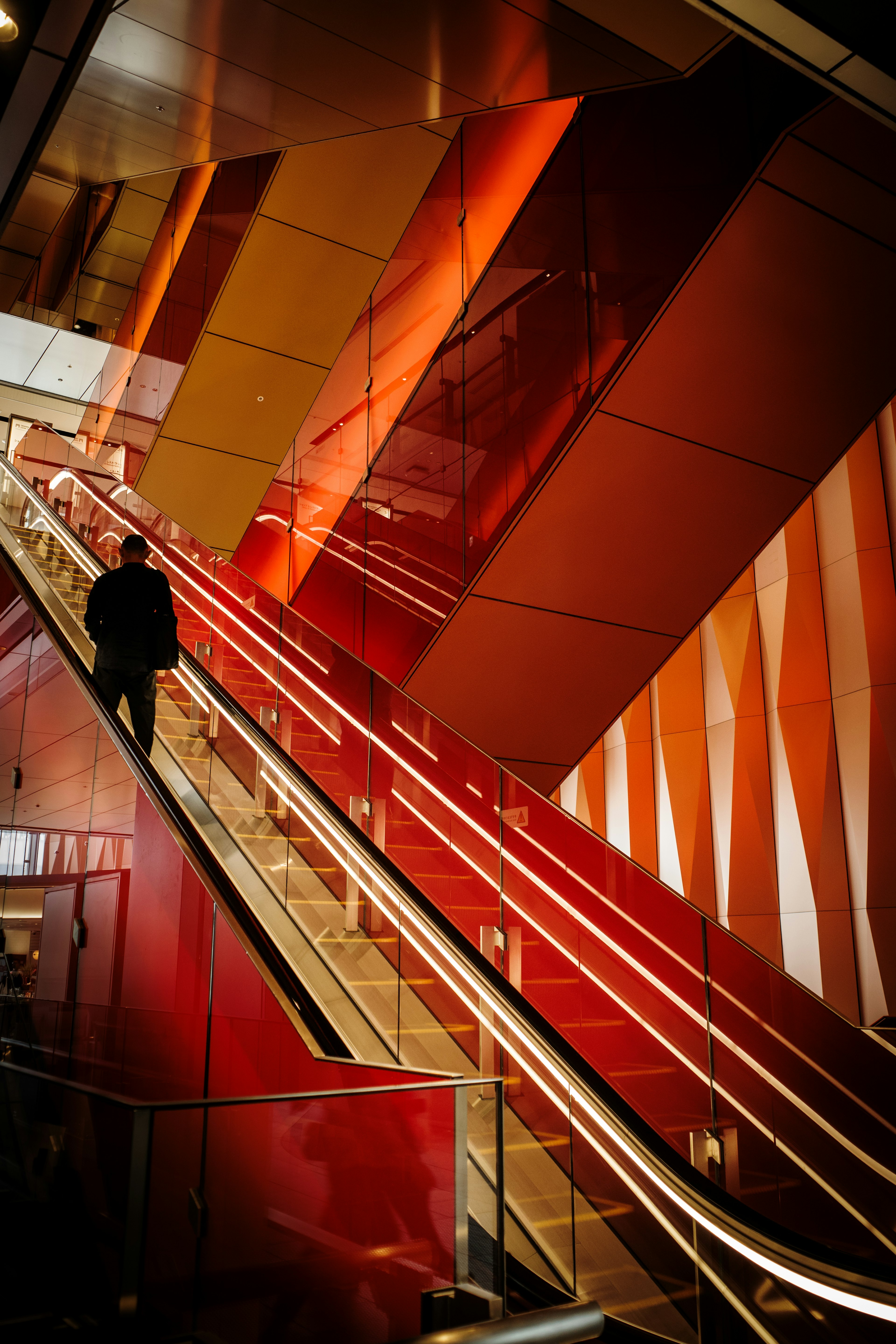 Person ascending escalator with red and orange angled walls