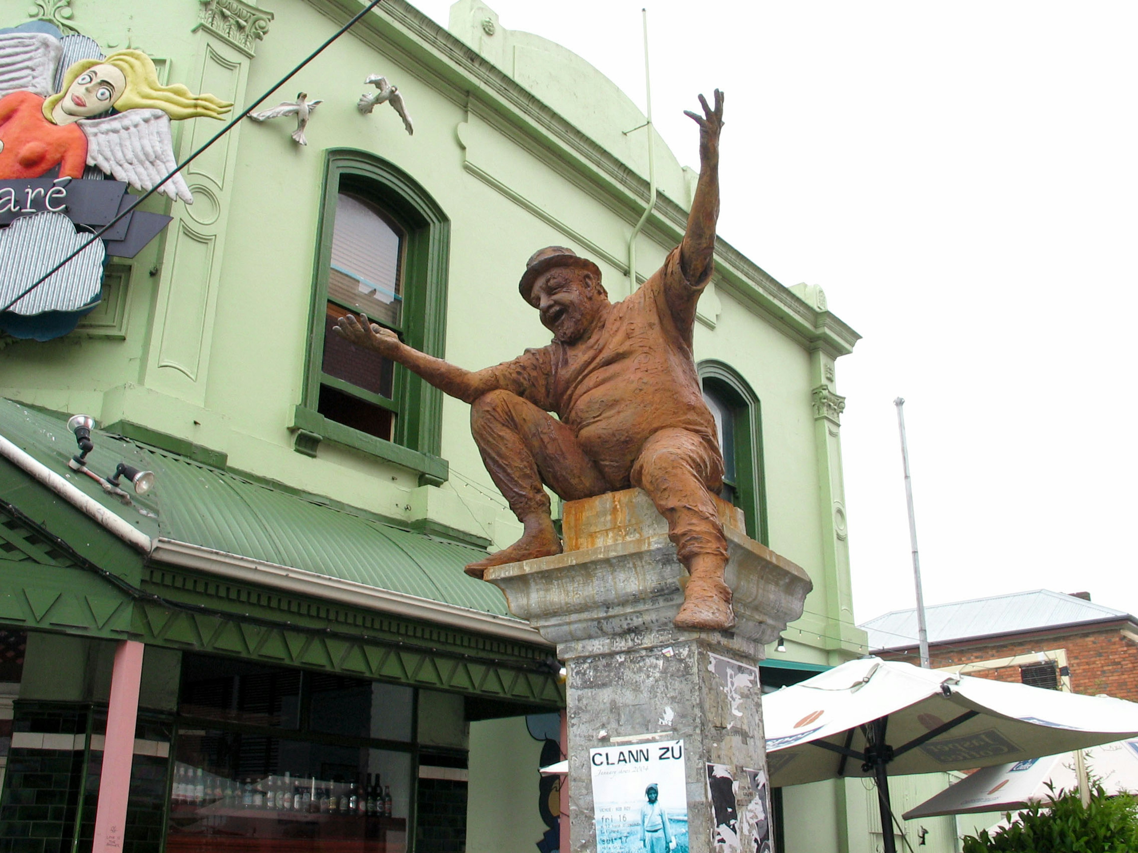 A humorous statue with arms raised in front of a green building