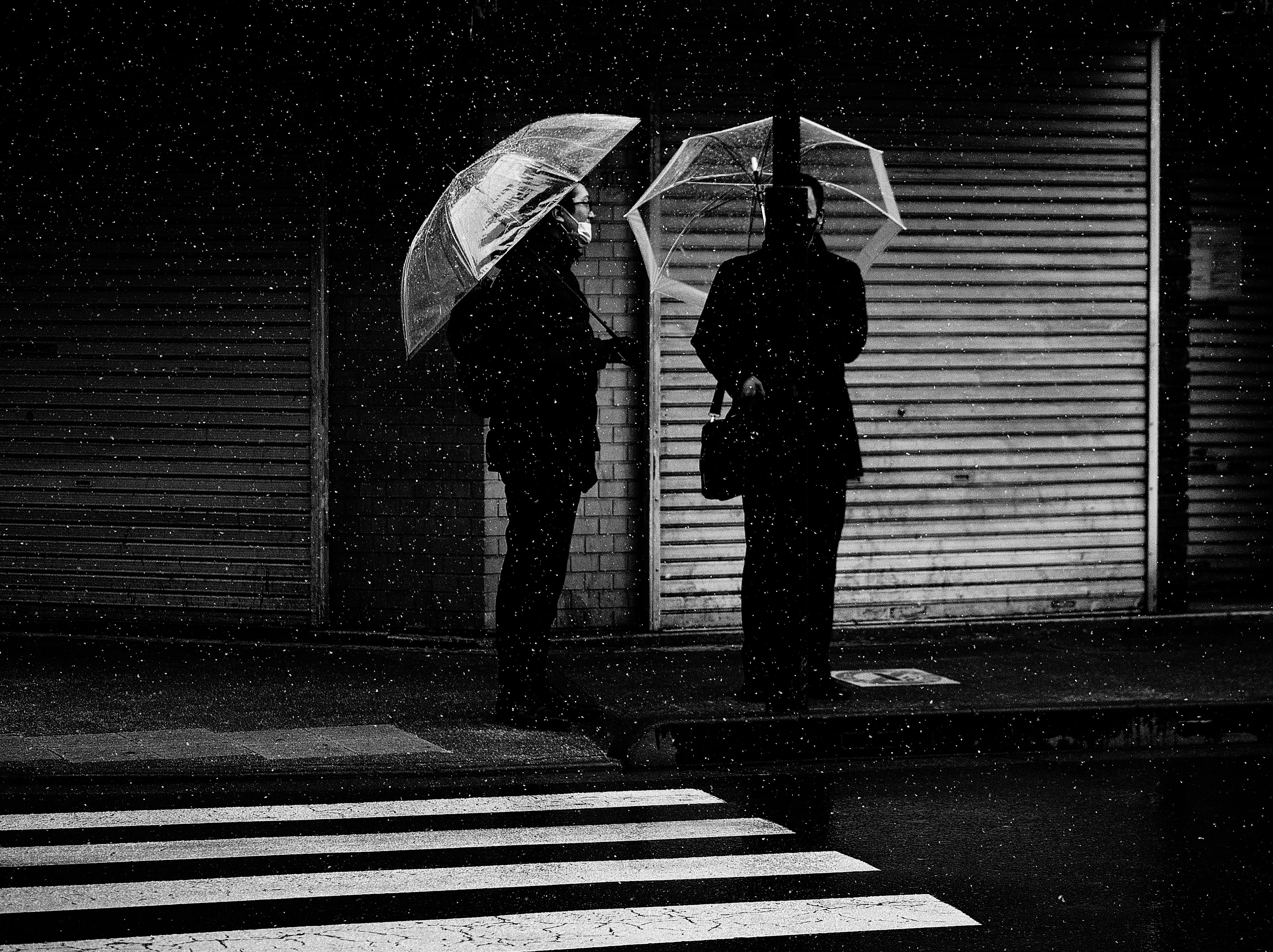 Two figures holding umbrellas in a monochrome setting with rain falling