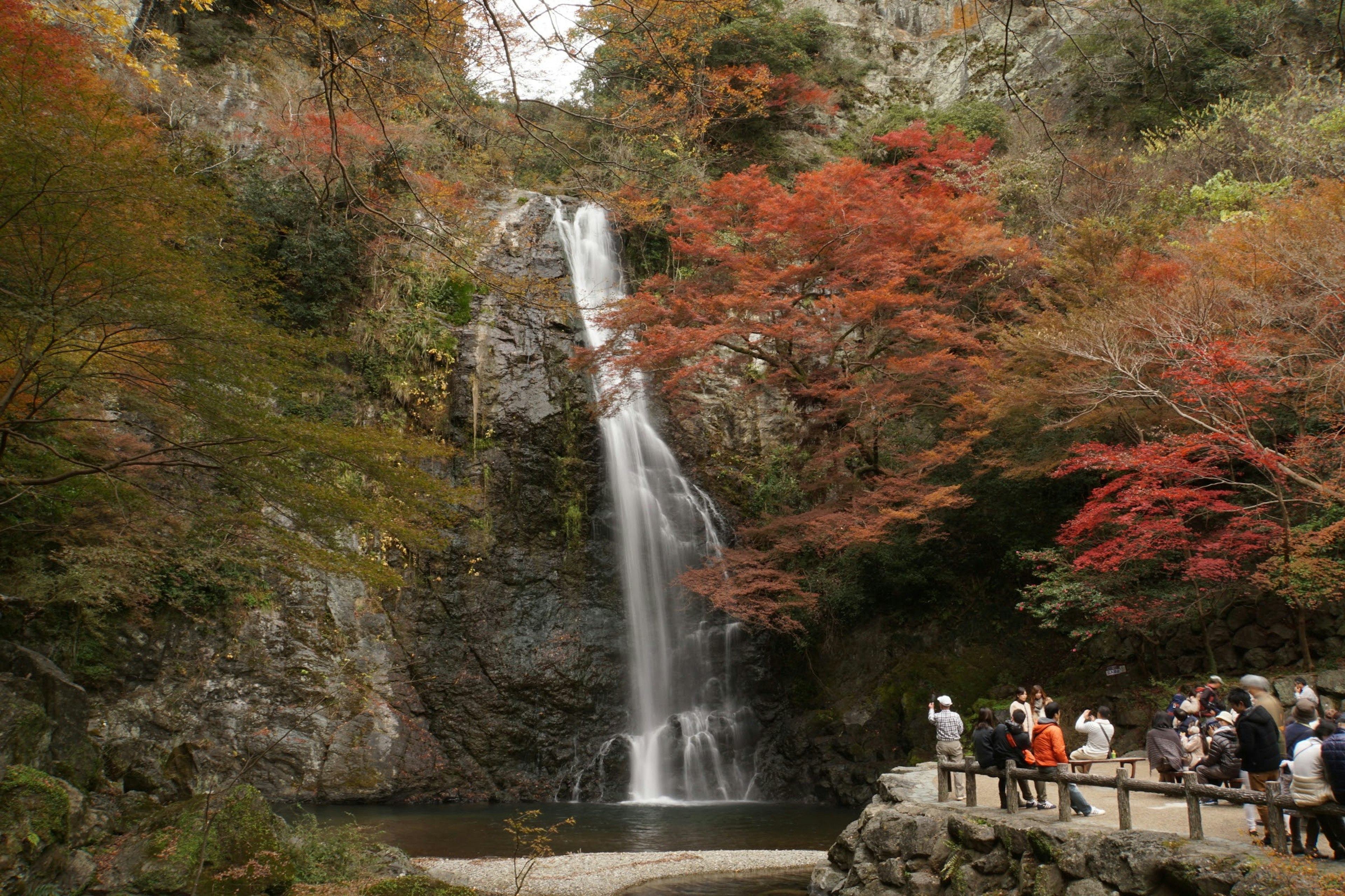 Cascada rodeada de follaje otoñal con visitantes