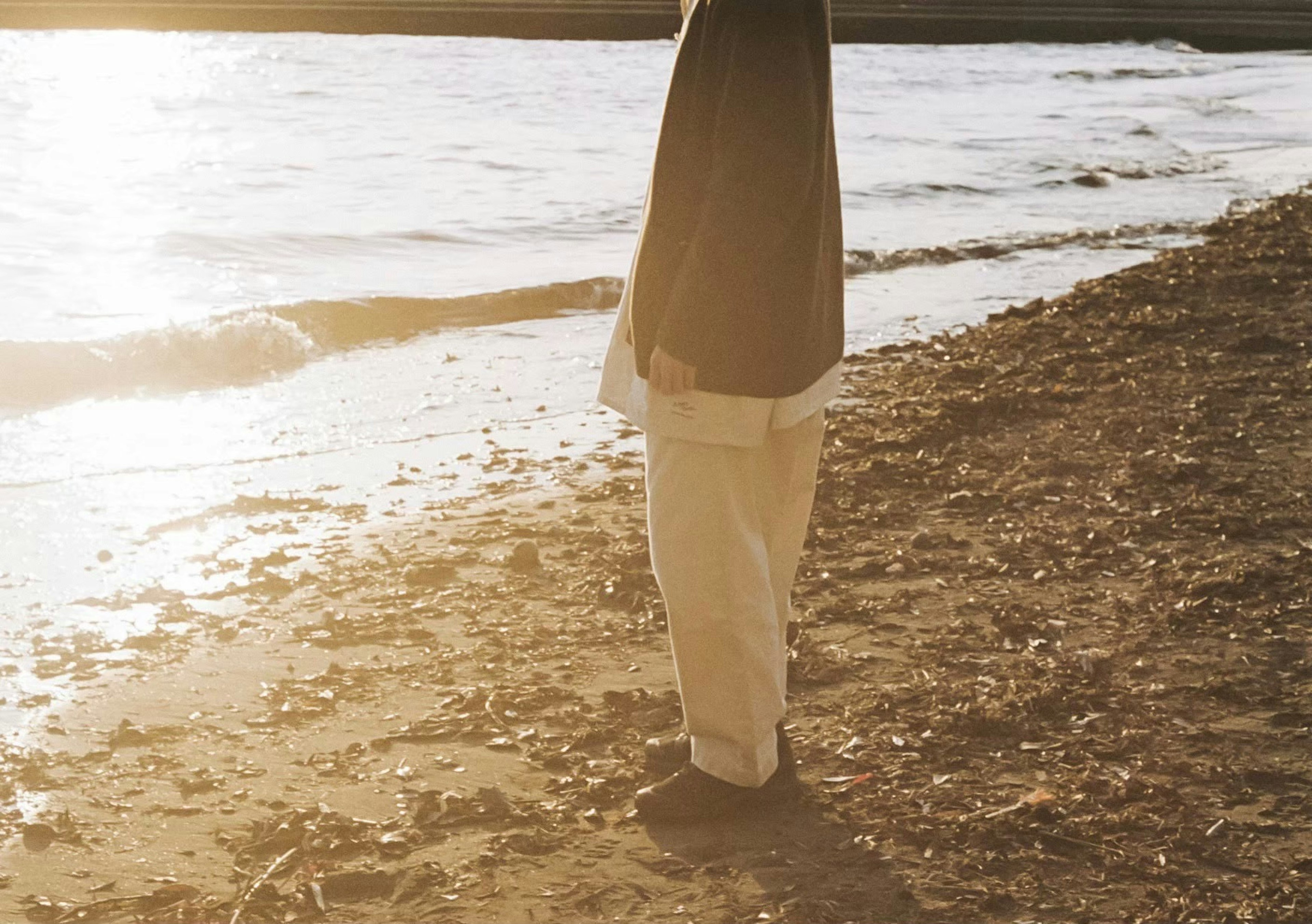 Person steht am Strand mit Sonnenlicht, das sich auf dem Wasser spiegelt