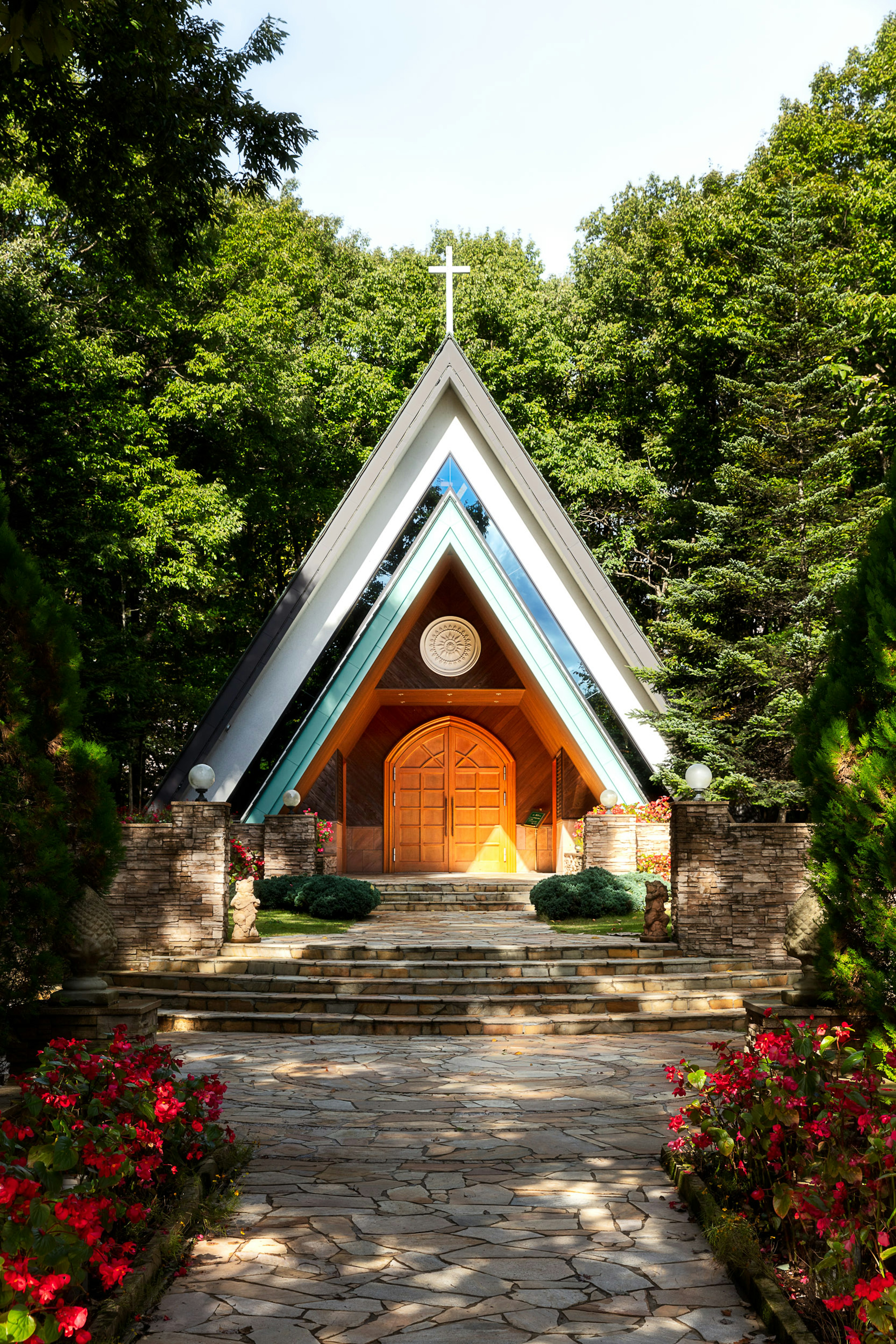 Modern church entrance surrounded by lush greenery featuring blue and white roof and vibrant flower beds