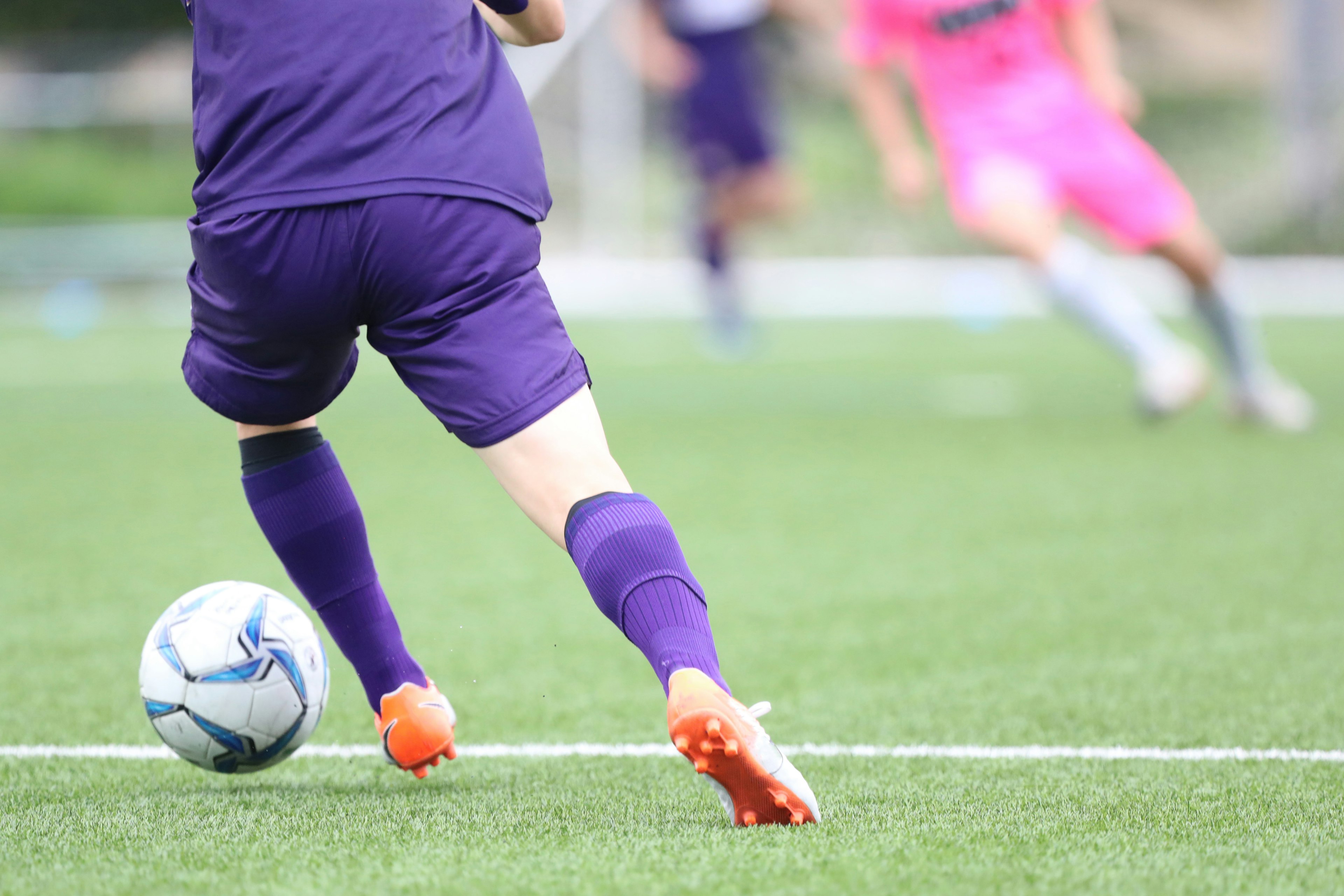 Spieler in lila Uniform, der auf einen Fußball auf dem Feld zuläuft