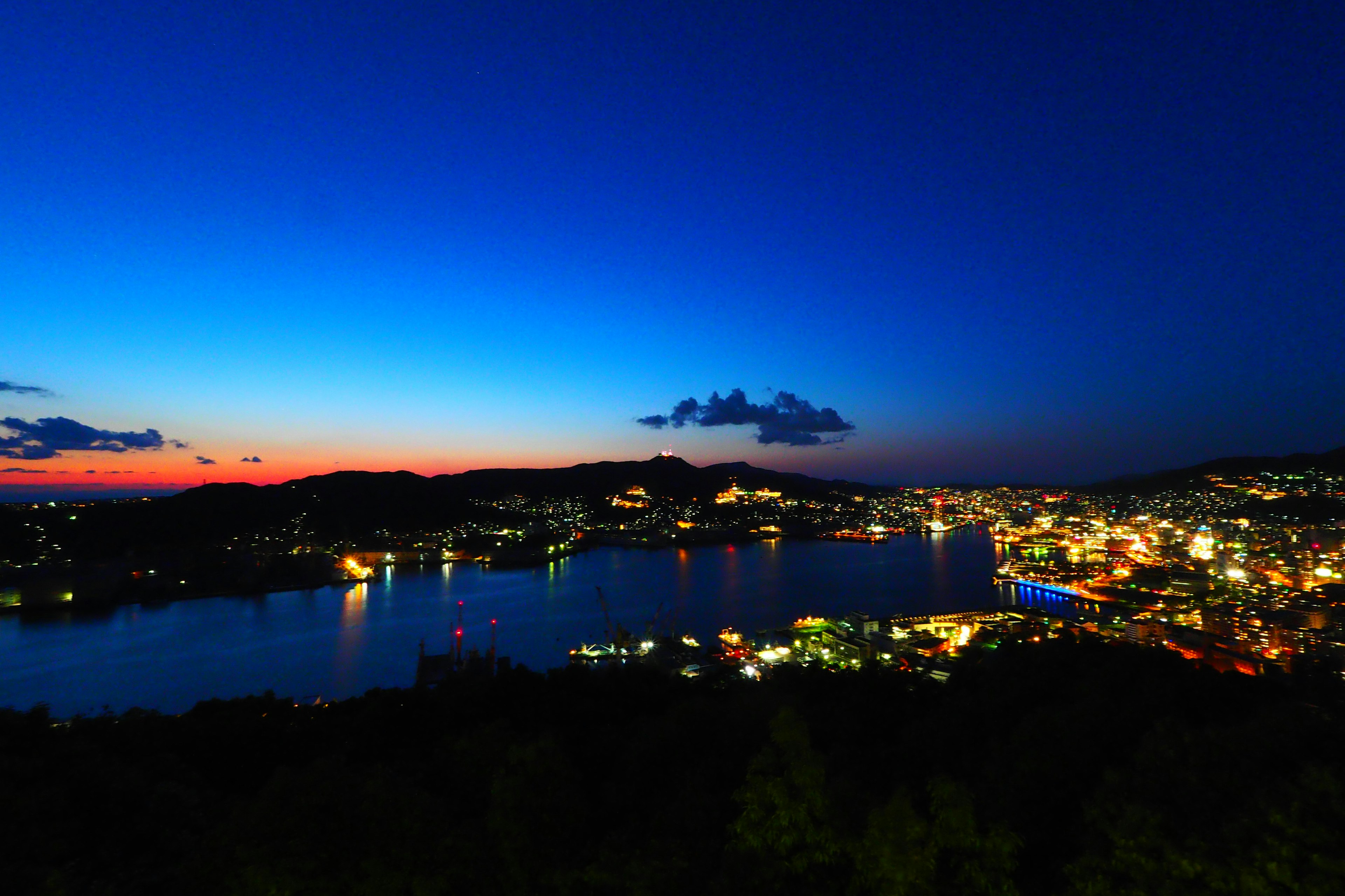 Belle vue nocturne d'une ville portuaire avec un ciel dégradé du bleu à l'orange et des lumières de la ville scintillantes