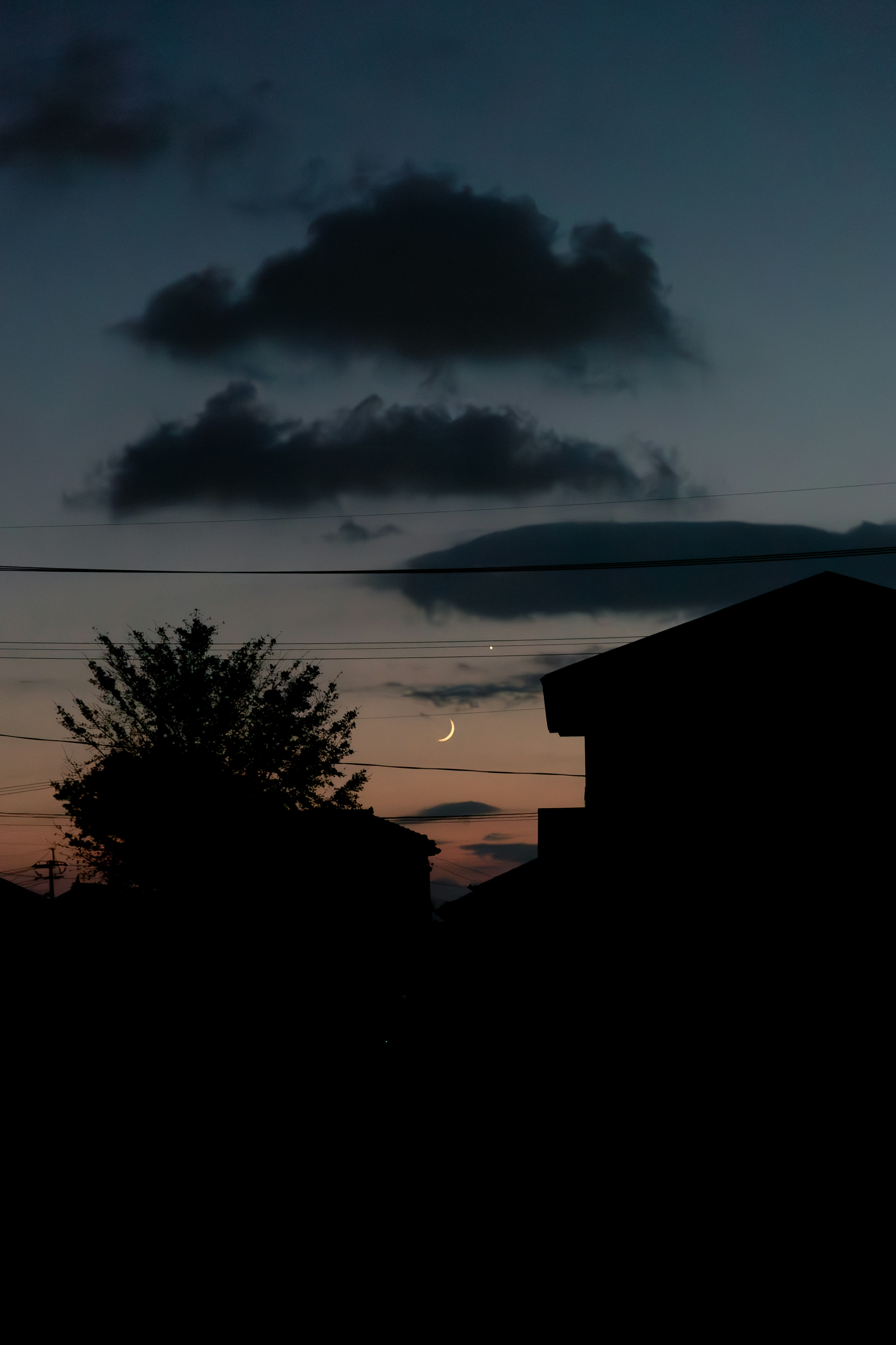 Silhouette di case contro un cielo al crepuscolo con una luna crescente