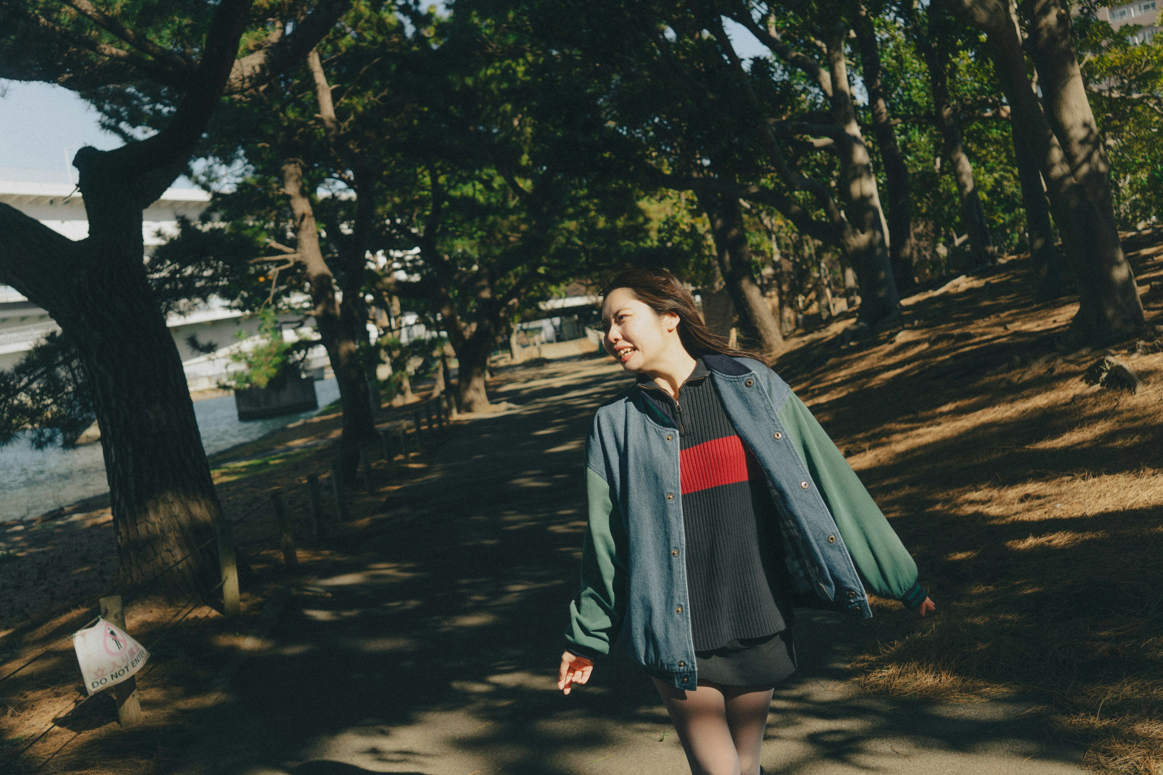 A woman walking on a park path wearing a green jacket and red sweater