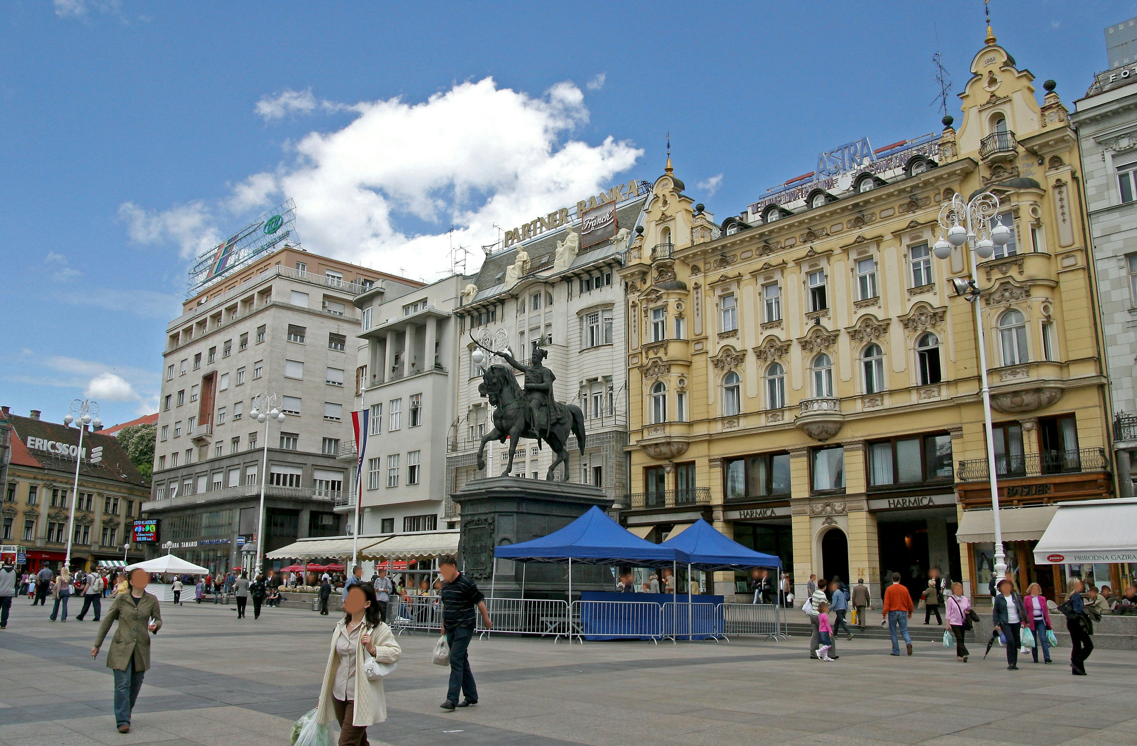 A scene of a square featuring an equestrian statue and surrounding buildings with people walking