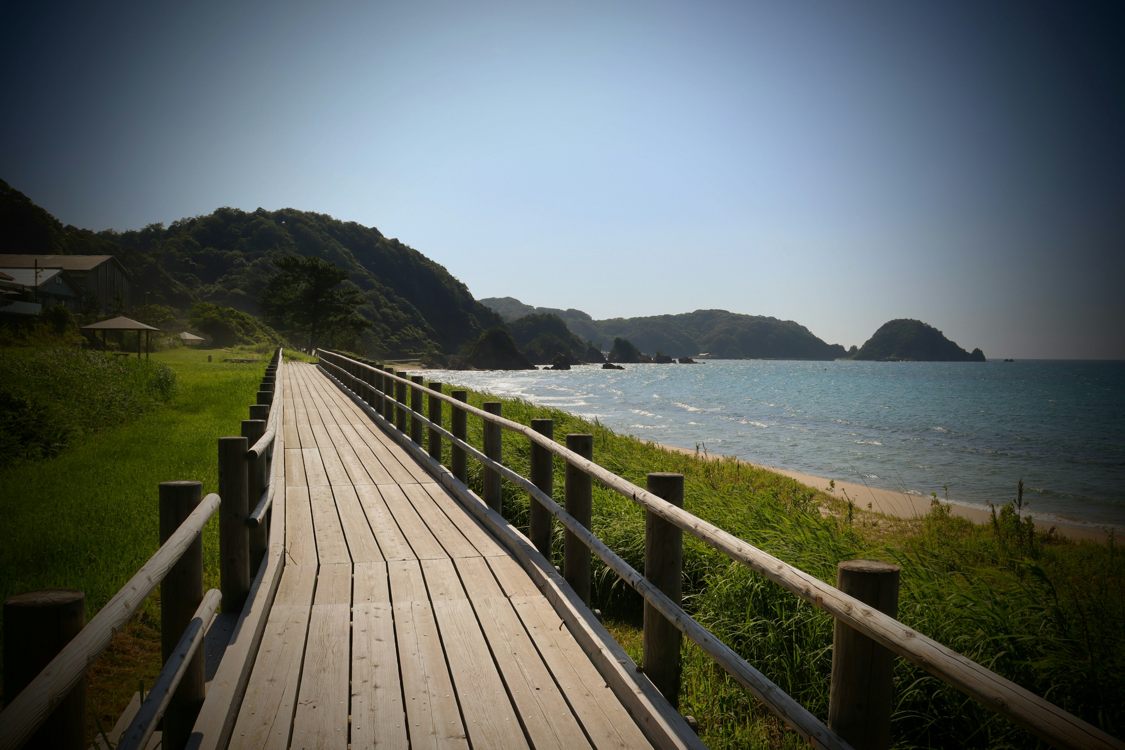 Jalan setapak kayu di sepanjang pantai dengan bukit dan laut