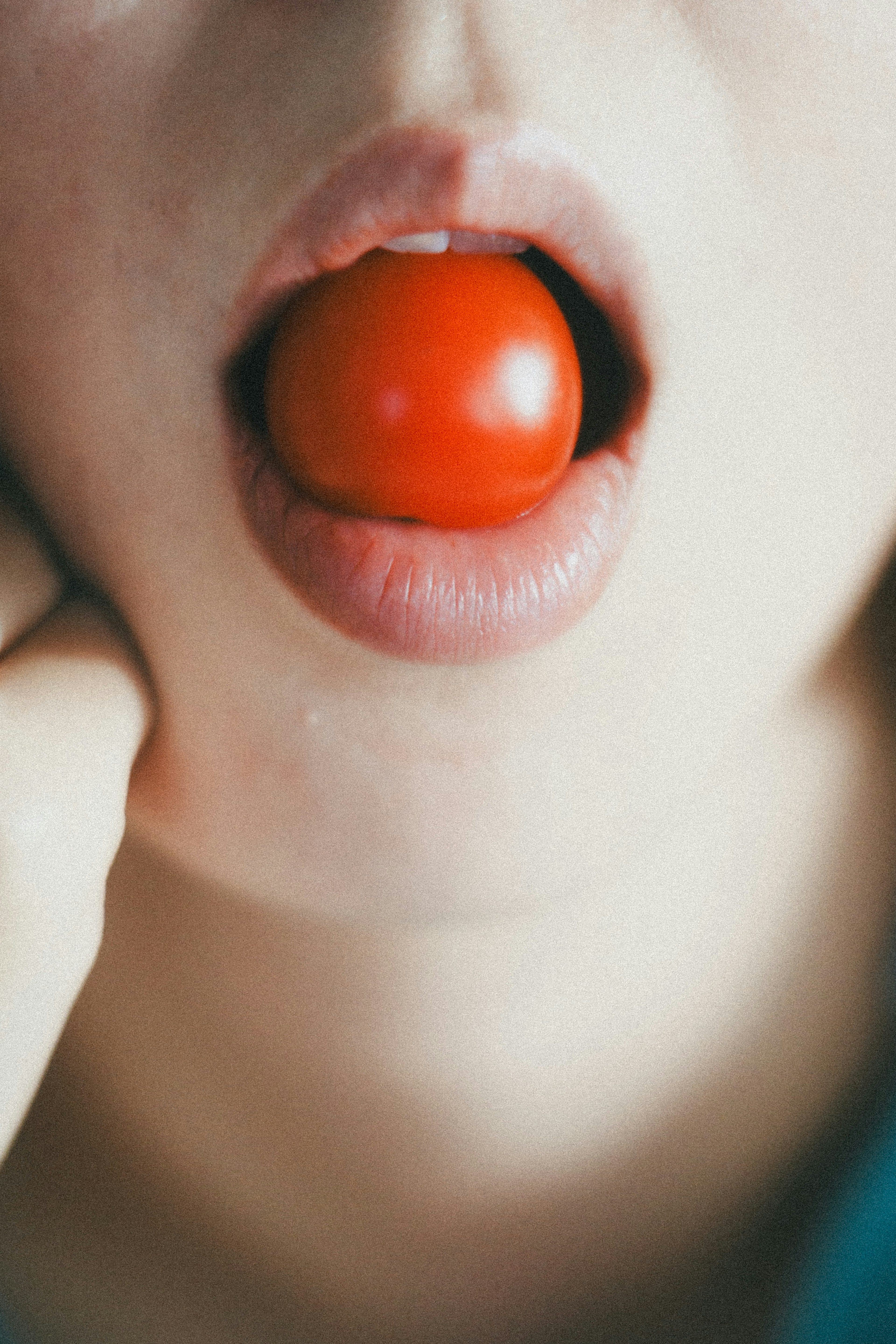 Close-up of a person's face with a cherry tomato in their mouth