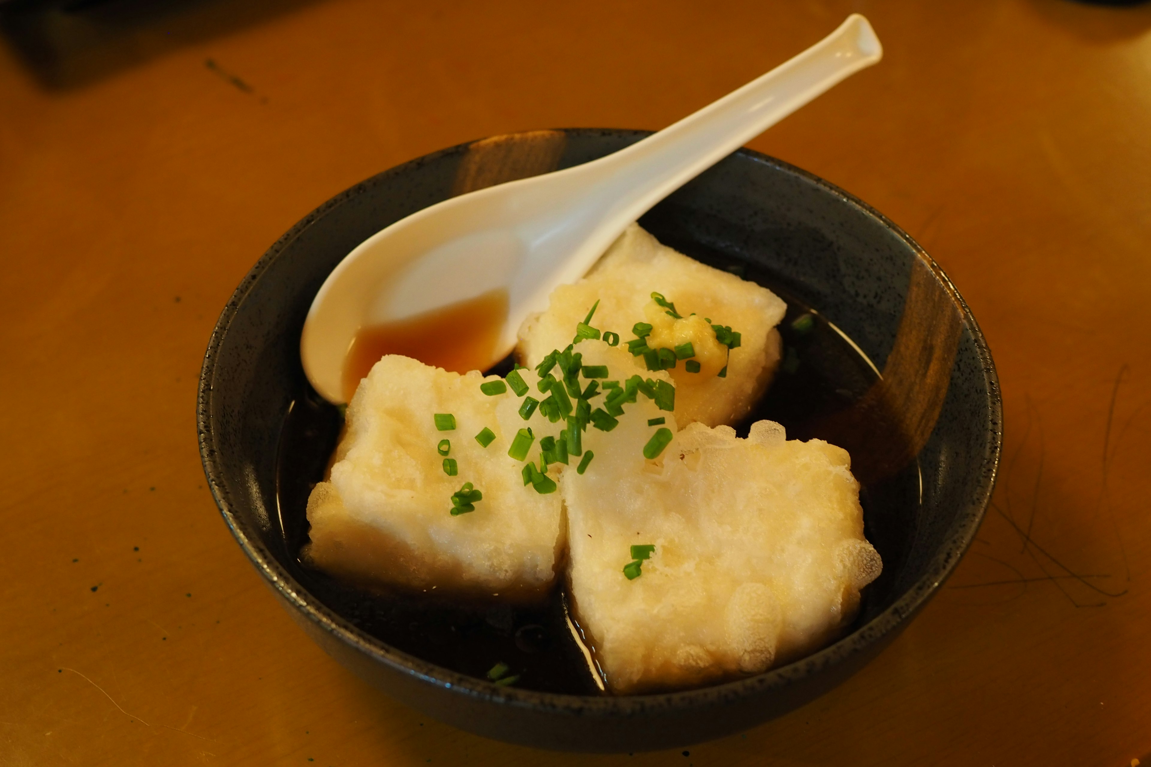 Drei Stücke Tofu in einer schwarzen Schüssel mit Frühlingszwiebeln garniert