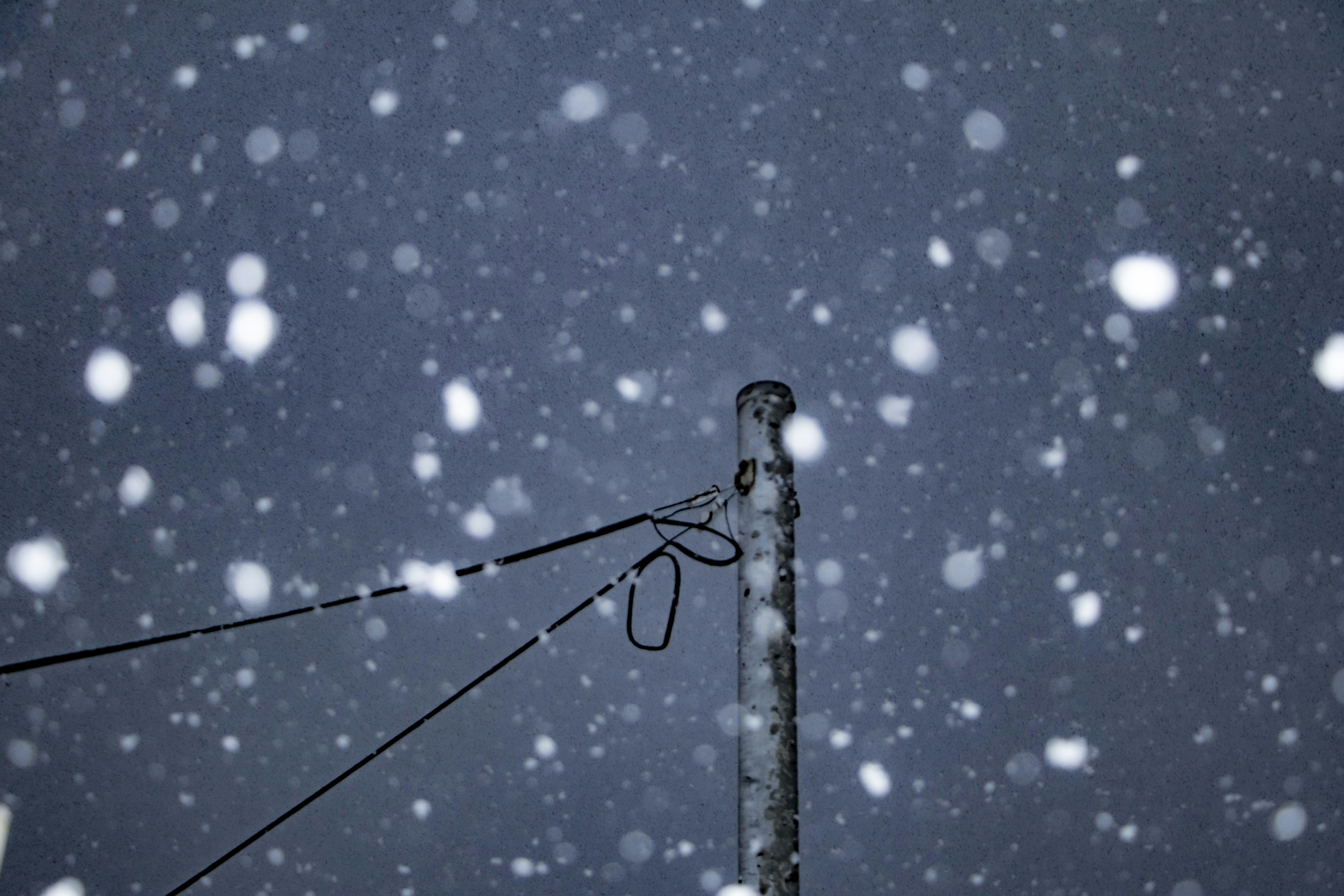 Una escena invernal con un poste de luz y cables en medio de una fuerte nevada