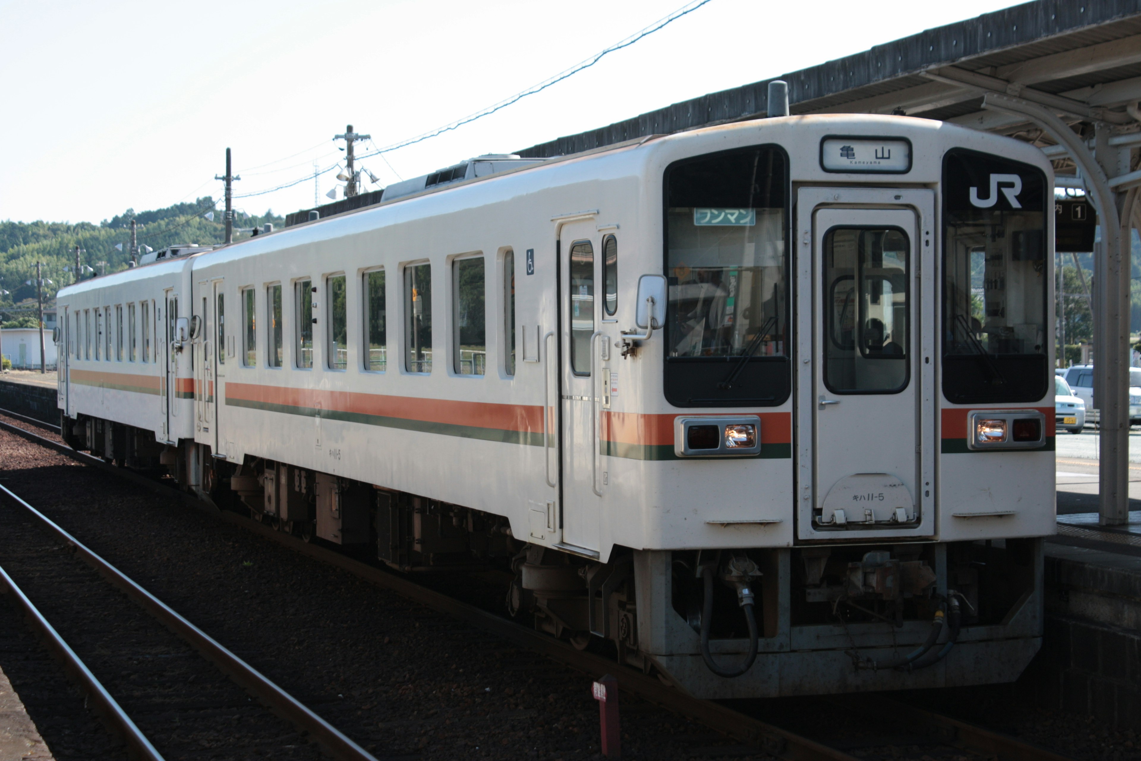 A white train with orange stripes parked at a station