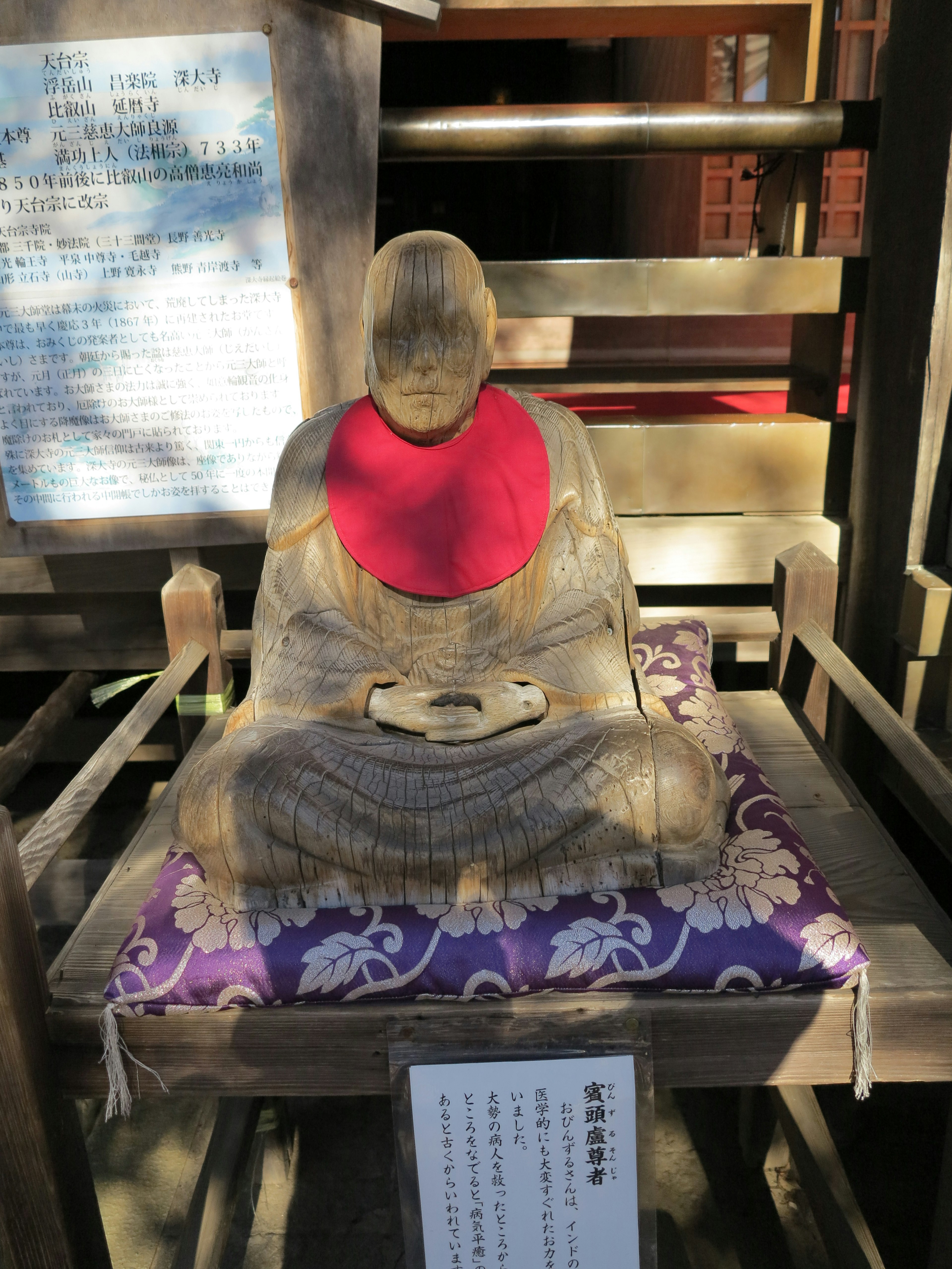 Buddha statue wearing a red bib seated on a purple cushion