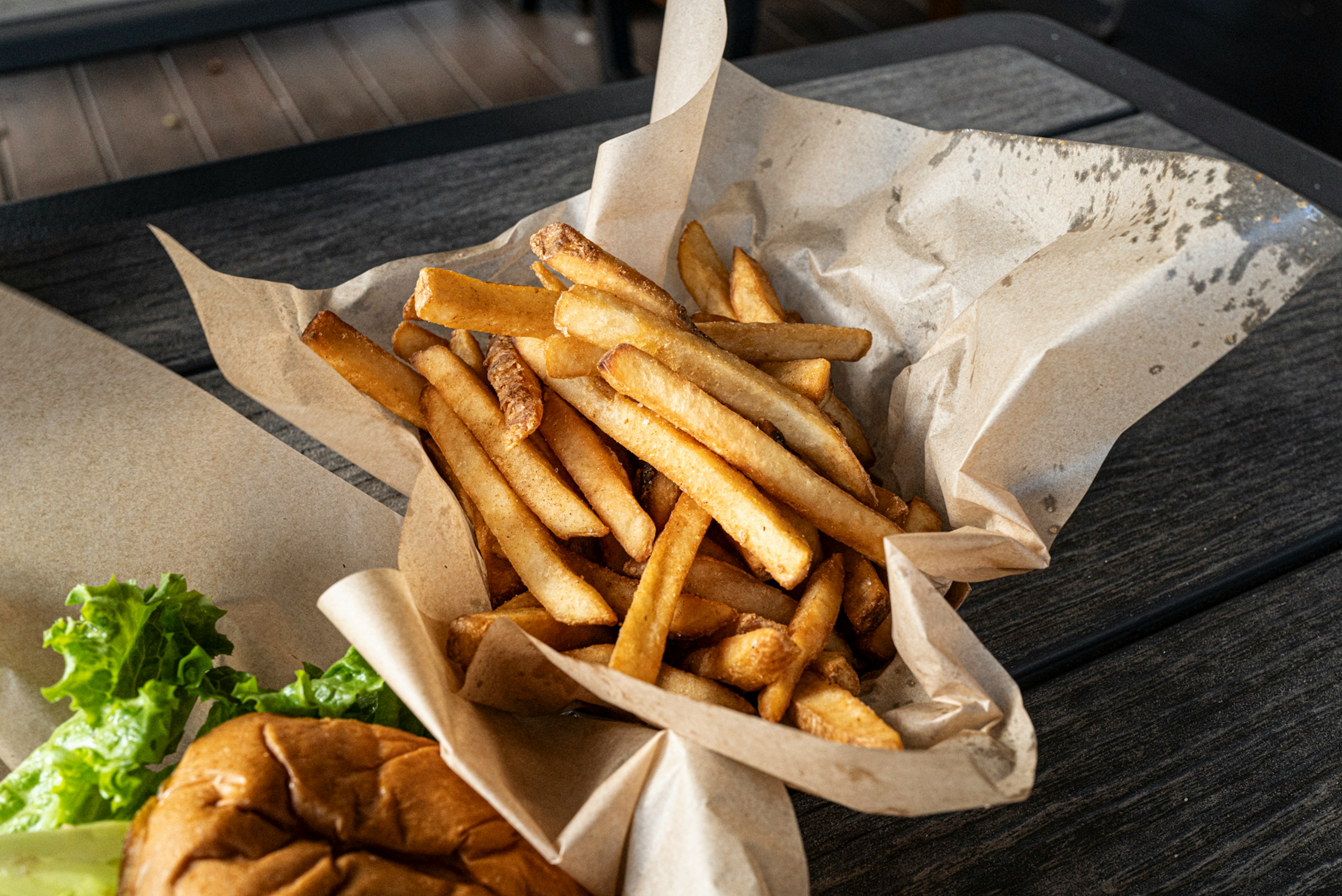 A serving of French fries in a paper container with a hamburger and lettuce nearby