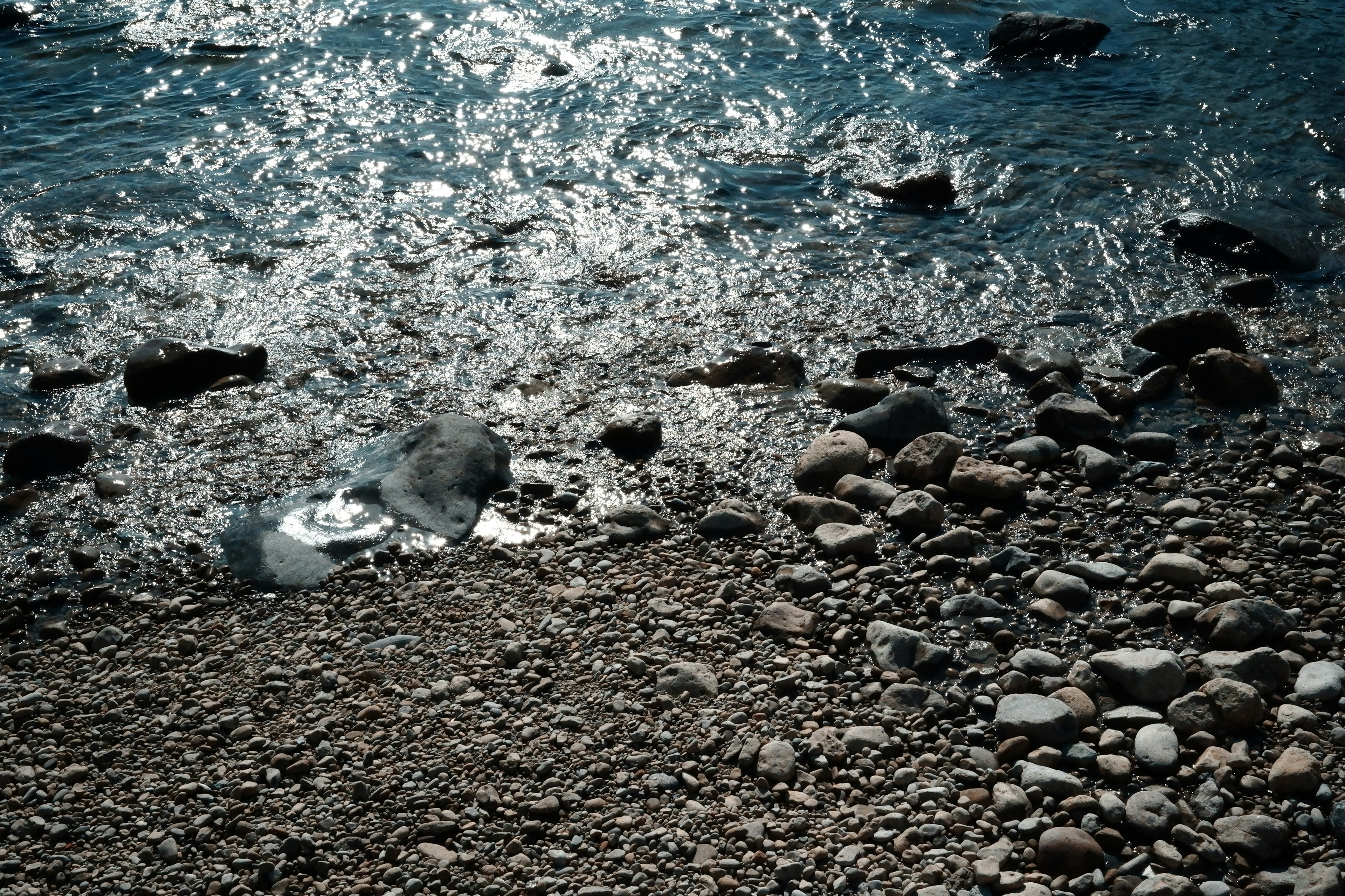 A shoreline with scattered stones and shimmering water surface