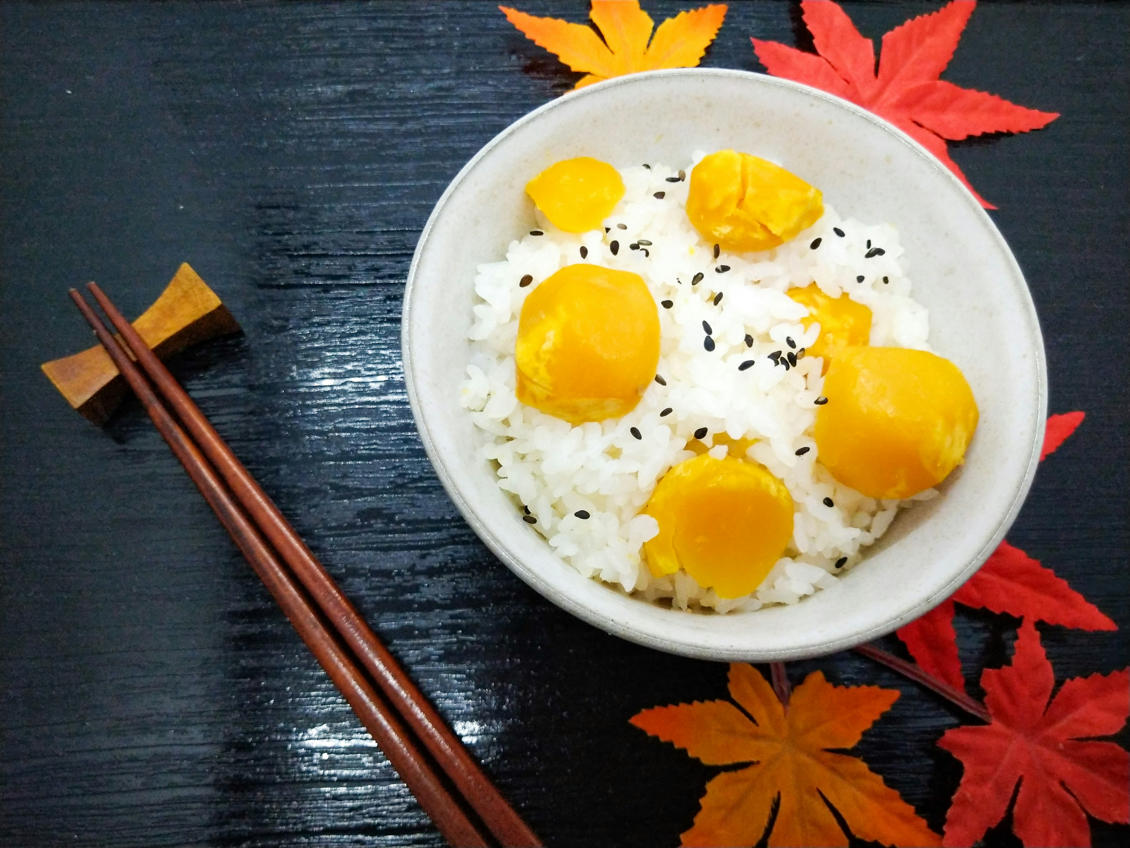 Mangkuk nasi putih dengan kuning telur di atasnya dikelilingi daun musim gugur