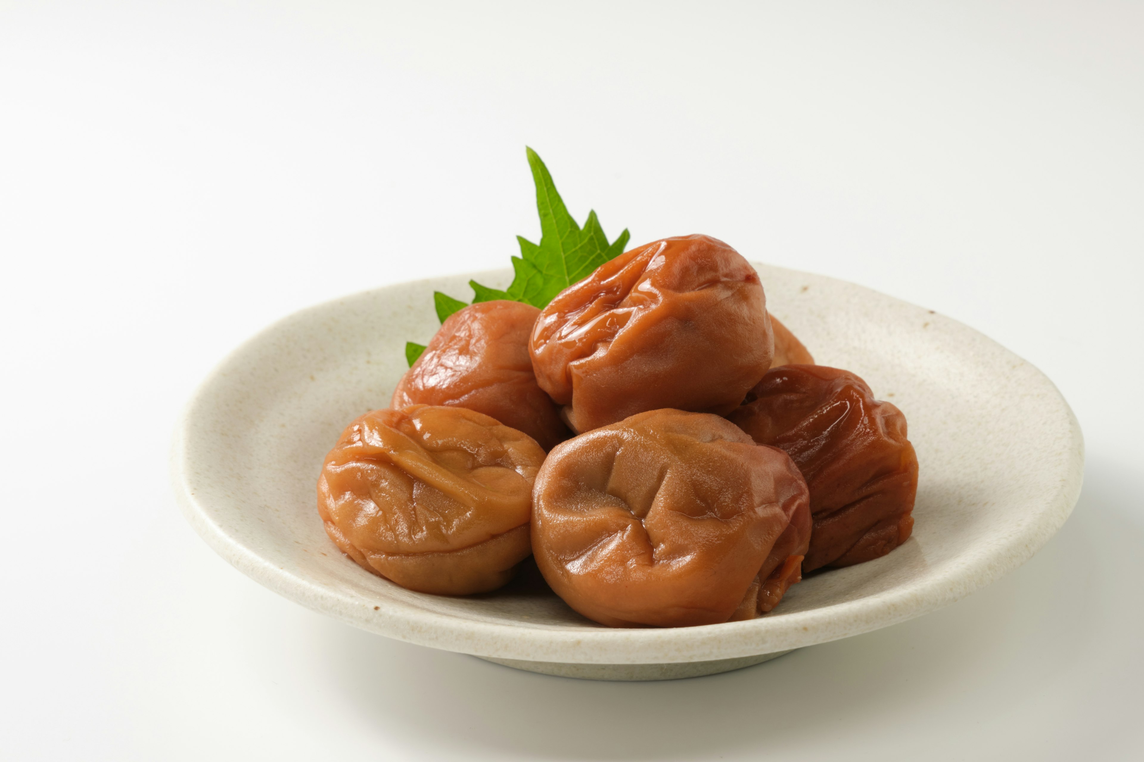 Ciruelas encurtidas dispuestas en un plato blanco con hojas de shiso