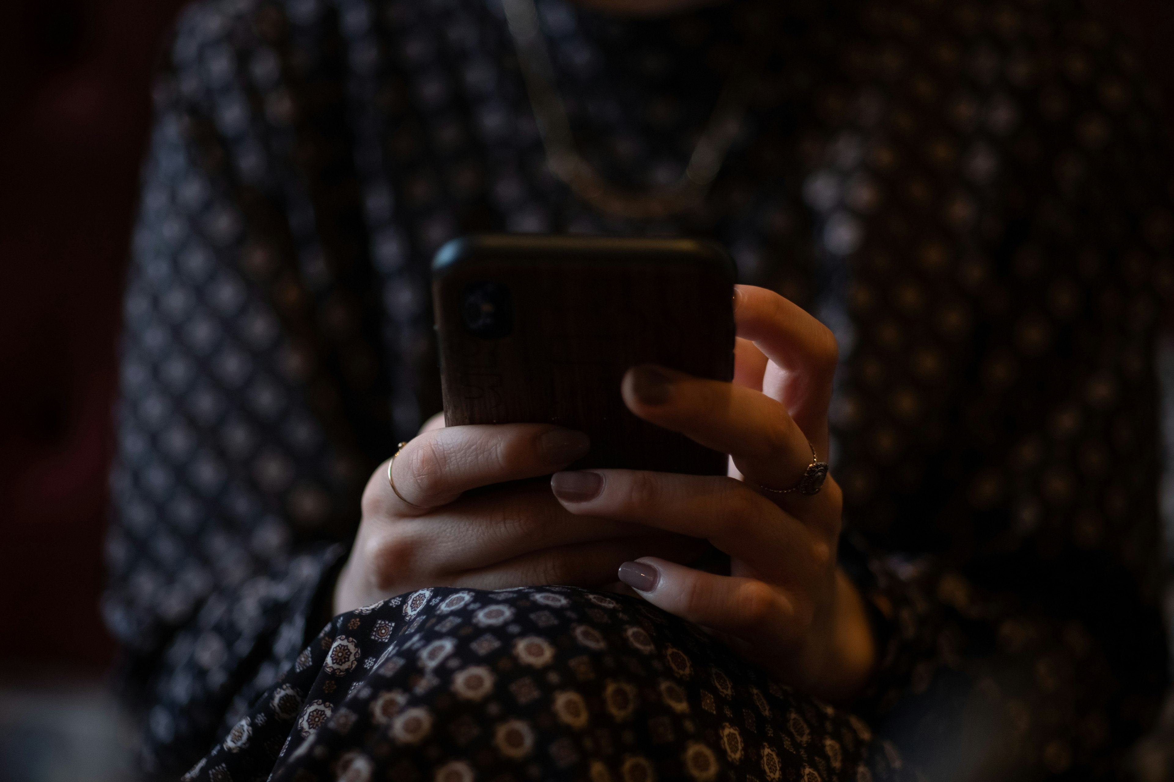 Primer plano de manos usando un smartphone con un sofá rojo difuminado de fondo