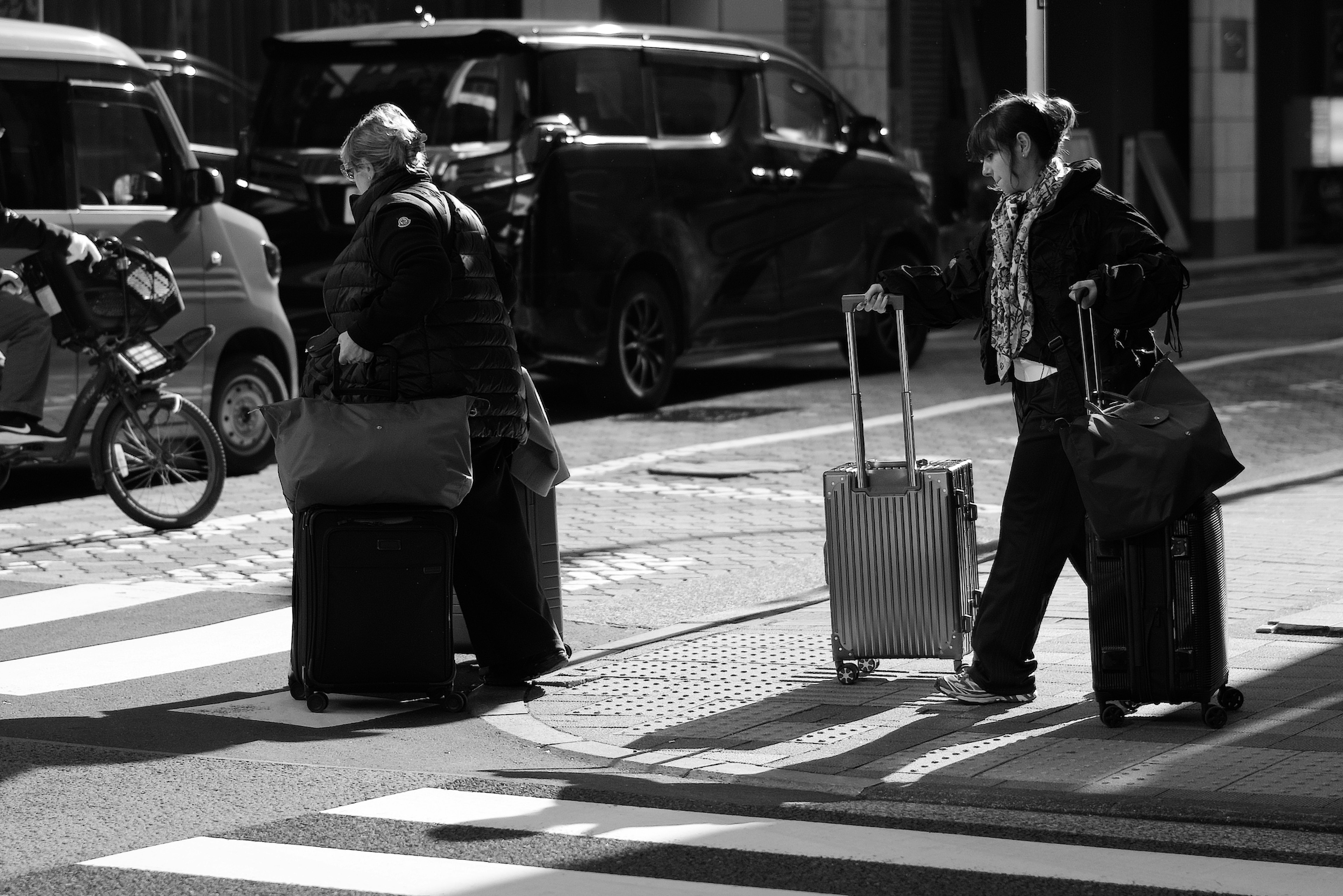 Two travelers with suitcases crossing a street in a black and white urban setting