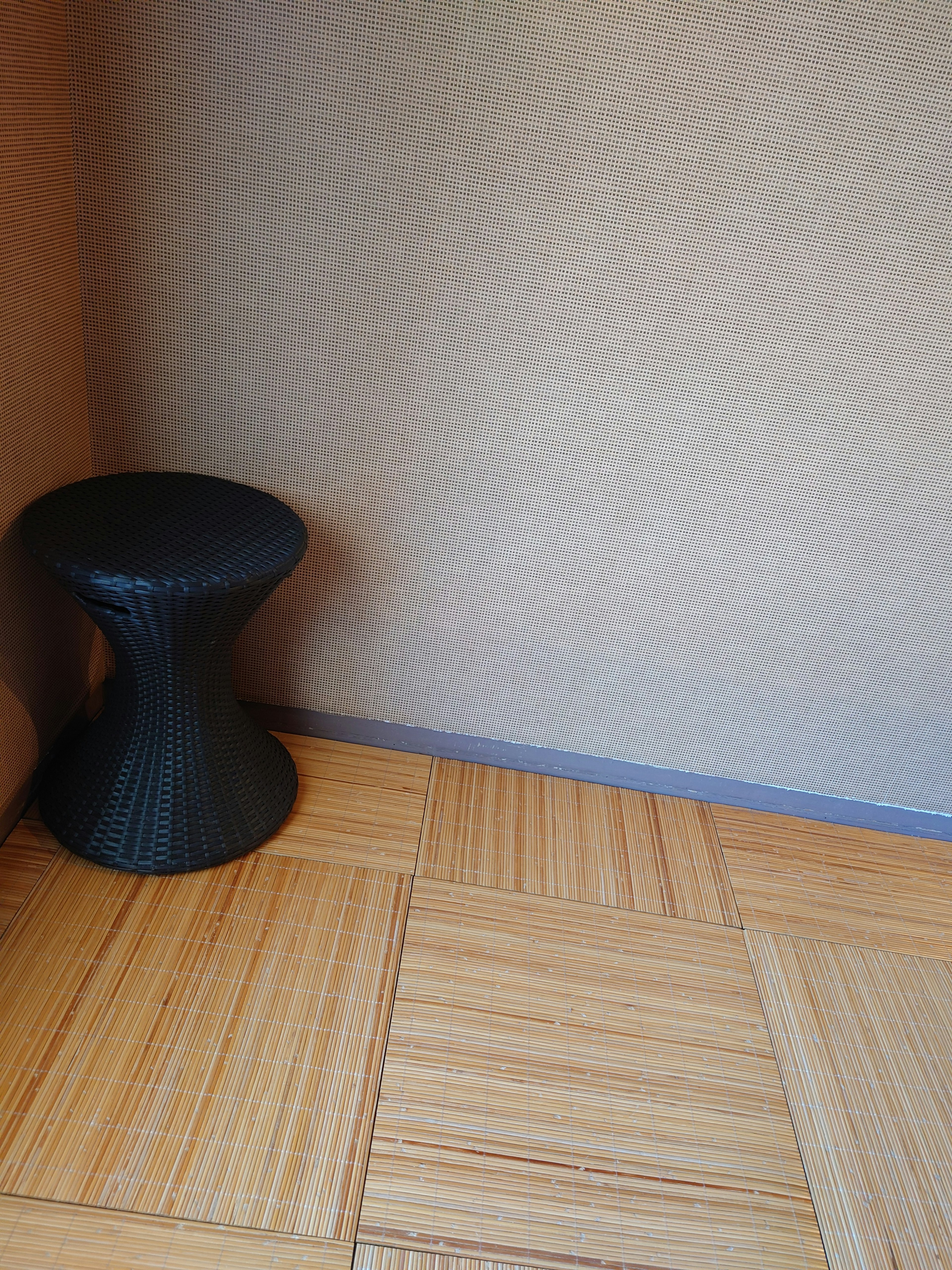 coin d'une pièce simple avec un tabouret noir et un sol en bois