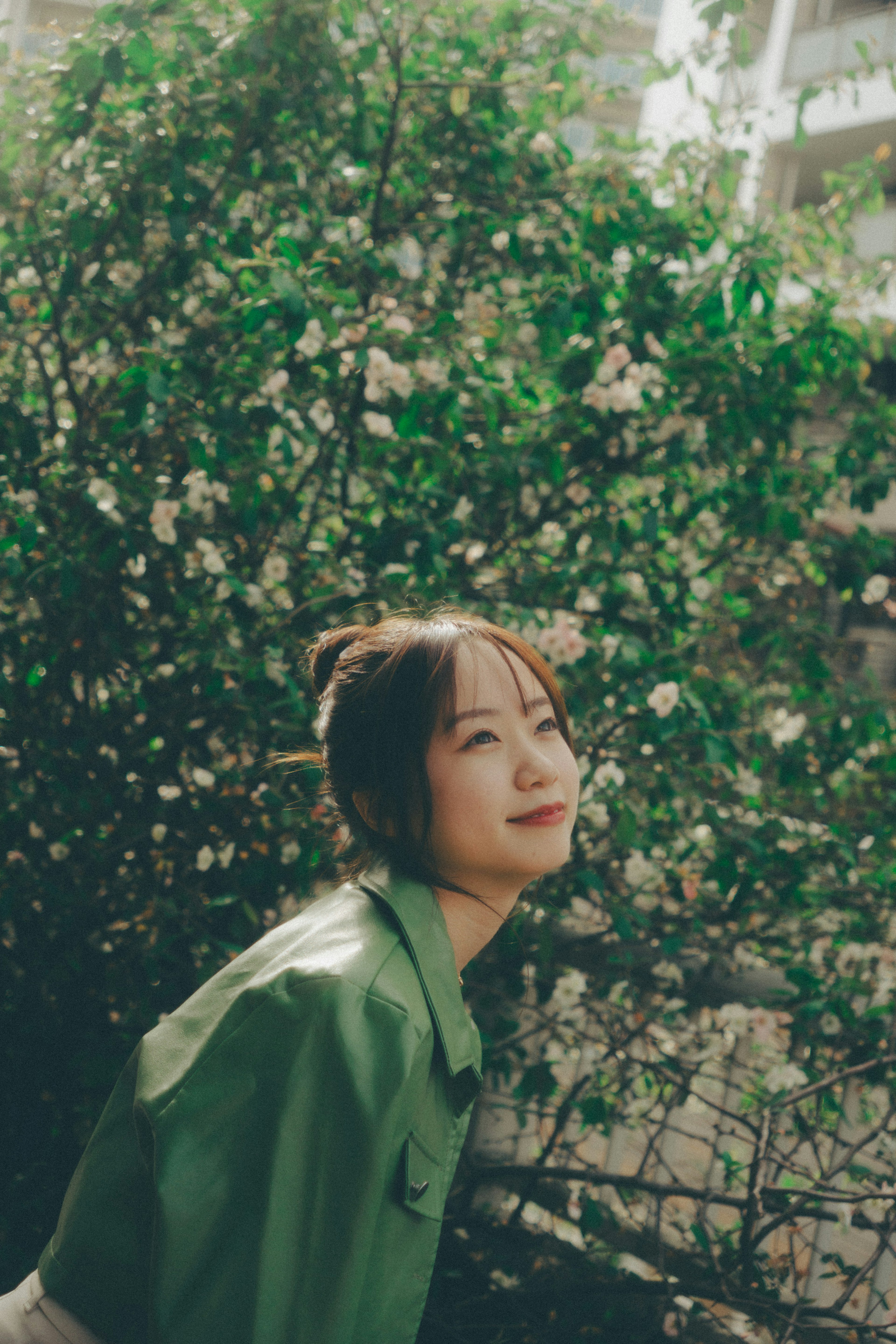 Une femme en chemise verte souriant devant un buisson fleuri