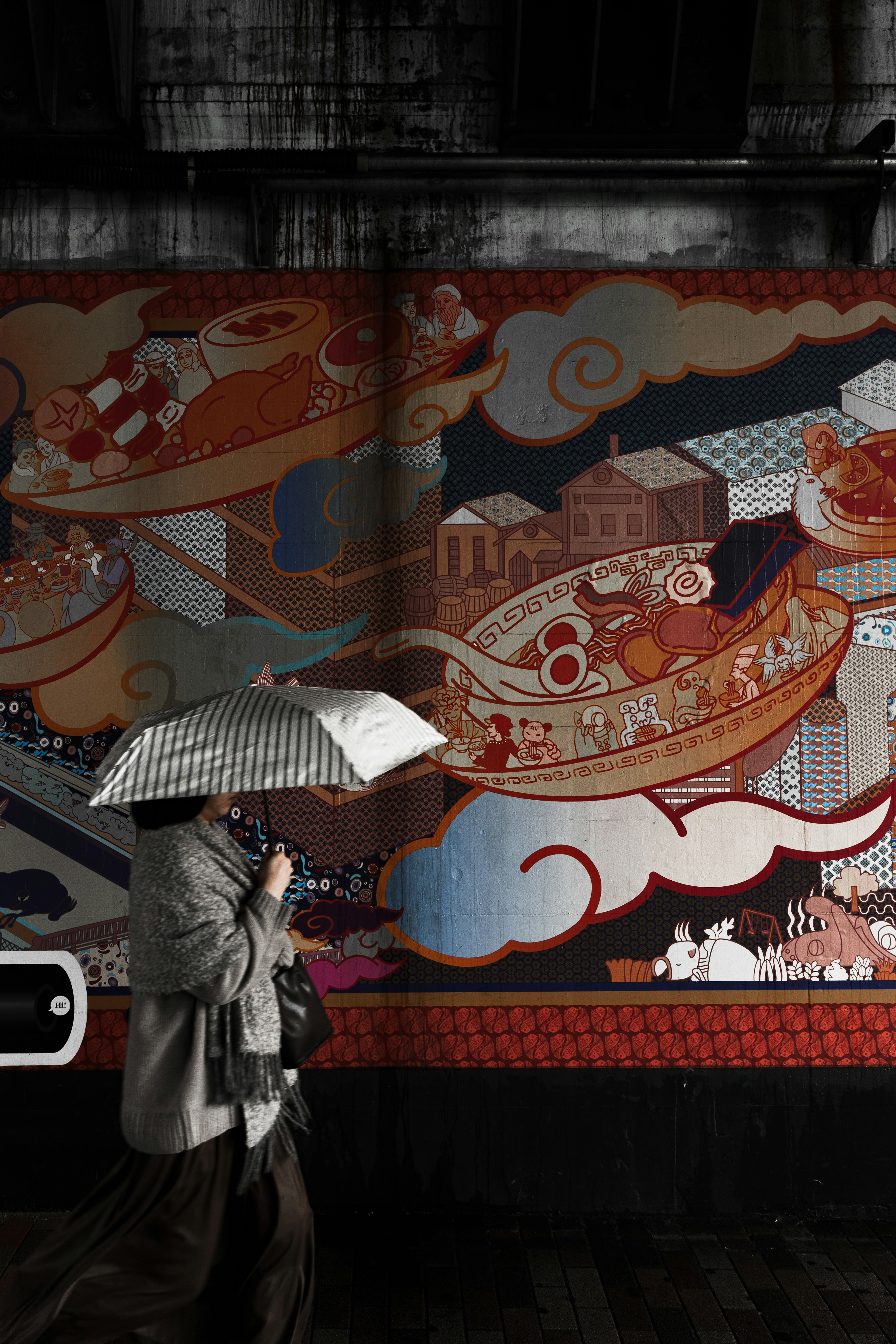 Person walking with an umbrella in front of a colorful mural