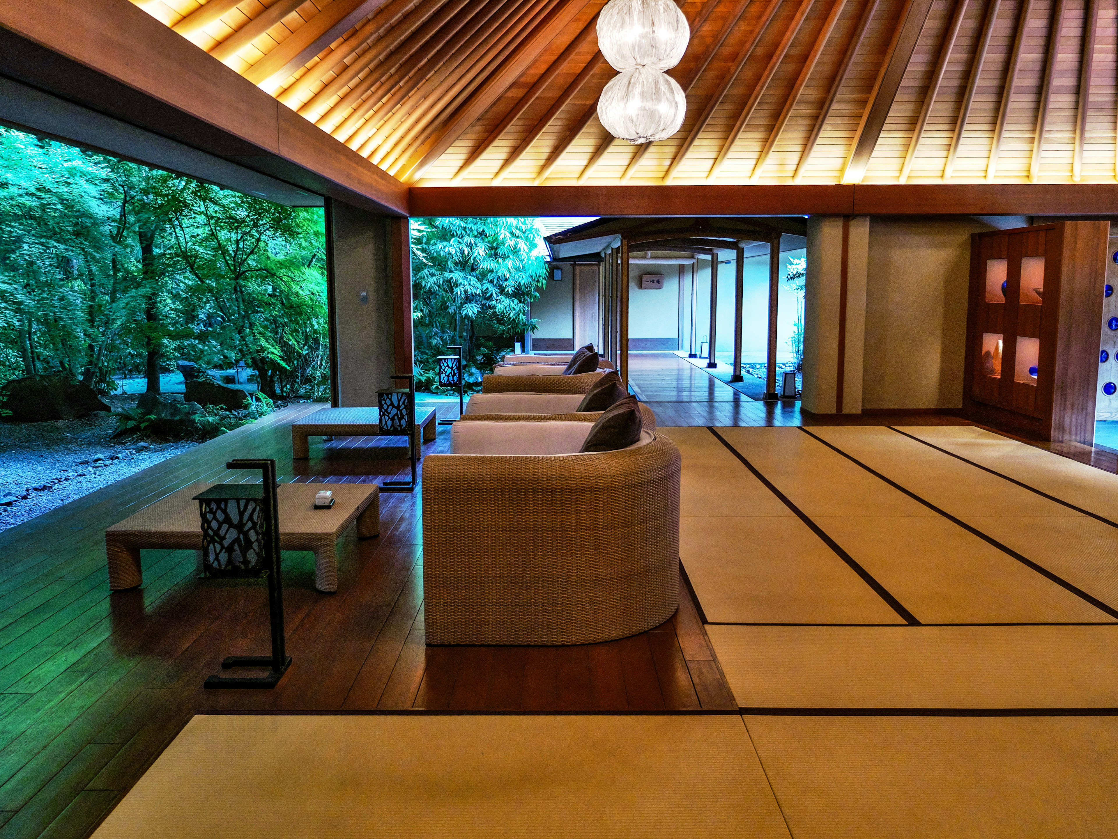 Interior de sala de estilo japonés techo de madera brillante sofás de colores relajantes grandes ventanas con vegetación exuberante