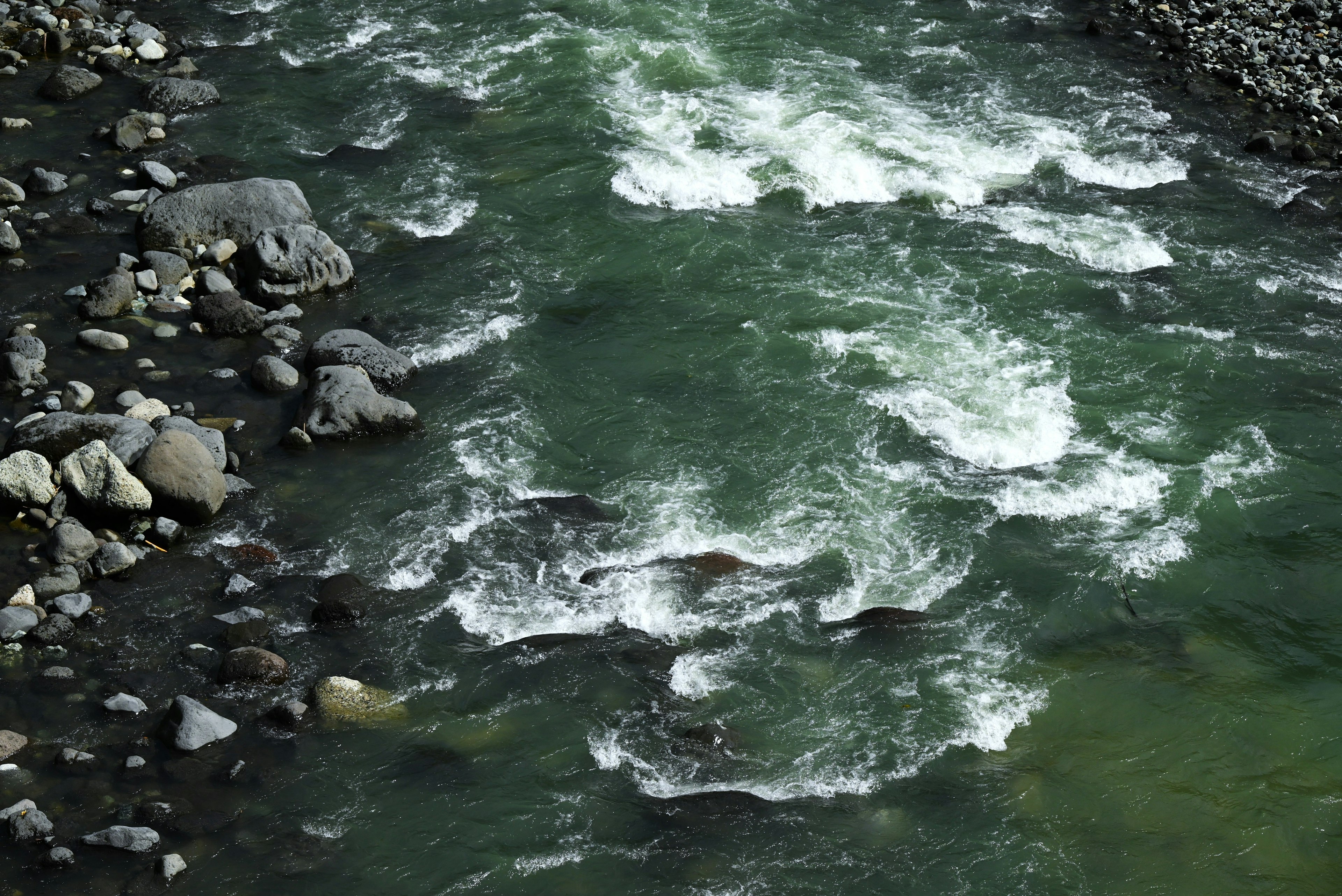 Luftaufnahme eines Flusses mit grünem Wasser und weißen schäumenden Wellen Steine und Felsen am Ufer