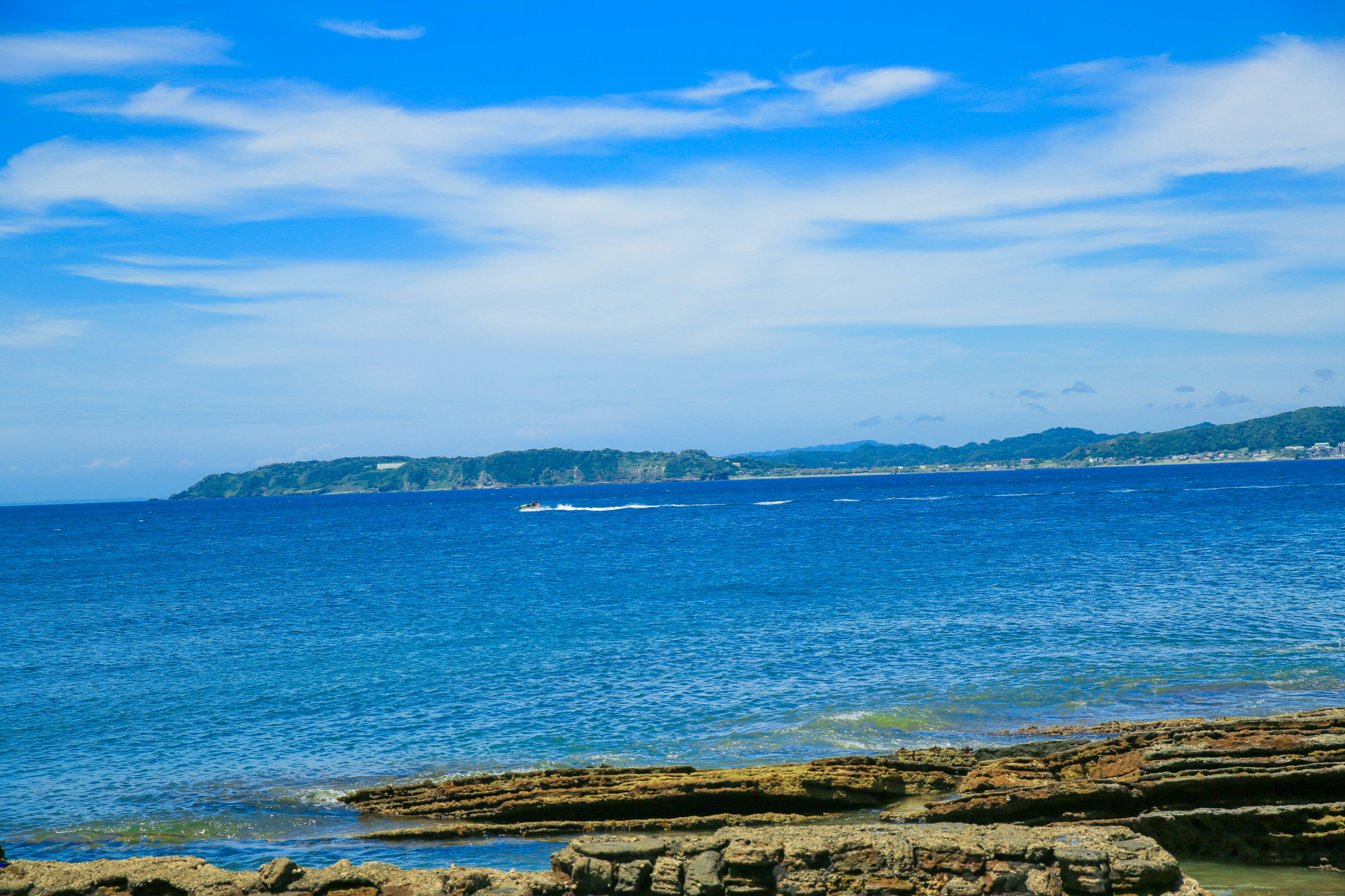 ทิวทัศน์ชายฝั่งที่มีทะเลสีน้ำเงินและชายหาดหิน มีเกาะอยู่ไกลออกไป