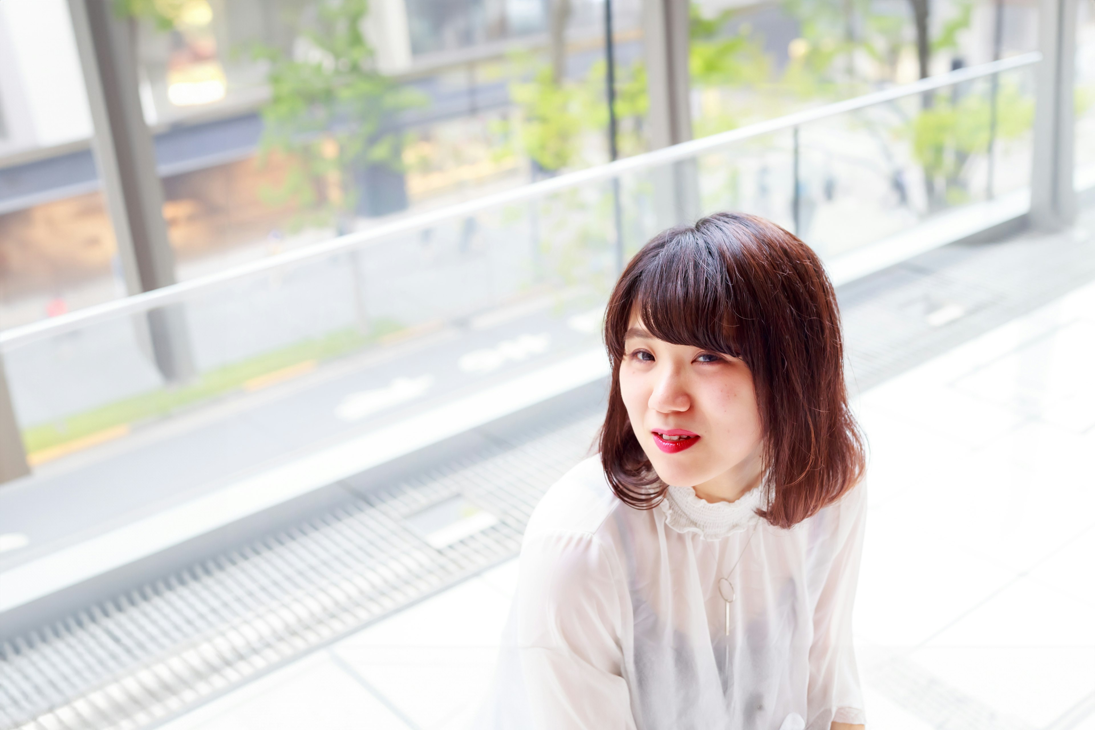 A woman smiling in a bright indoor setting wearing a white top