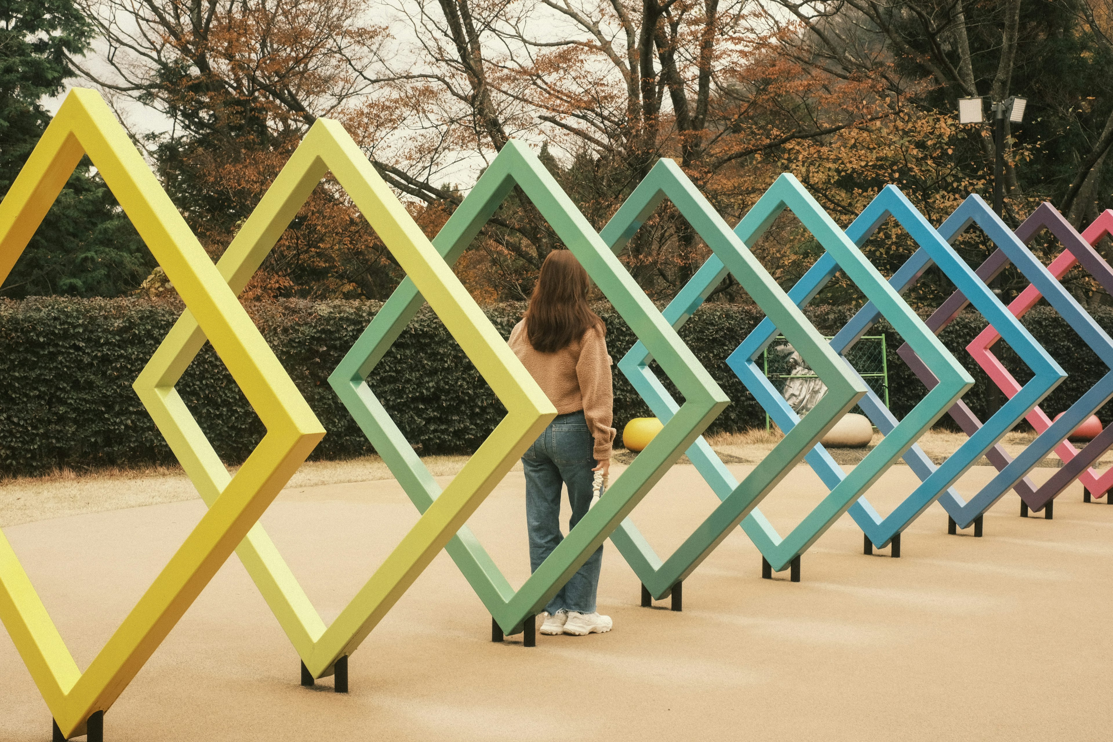 Una mujer de pie en un parque rodeada de marcos en forma de diamante coloridos