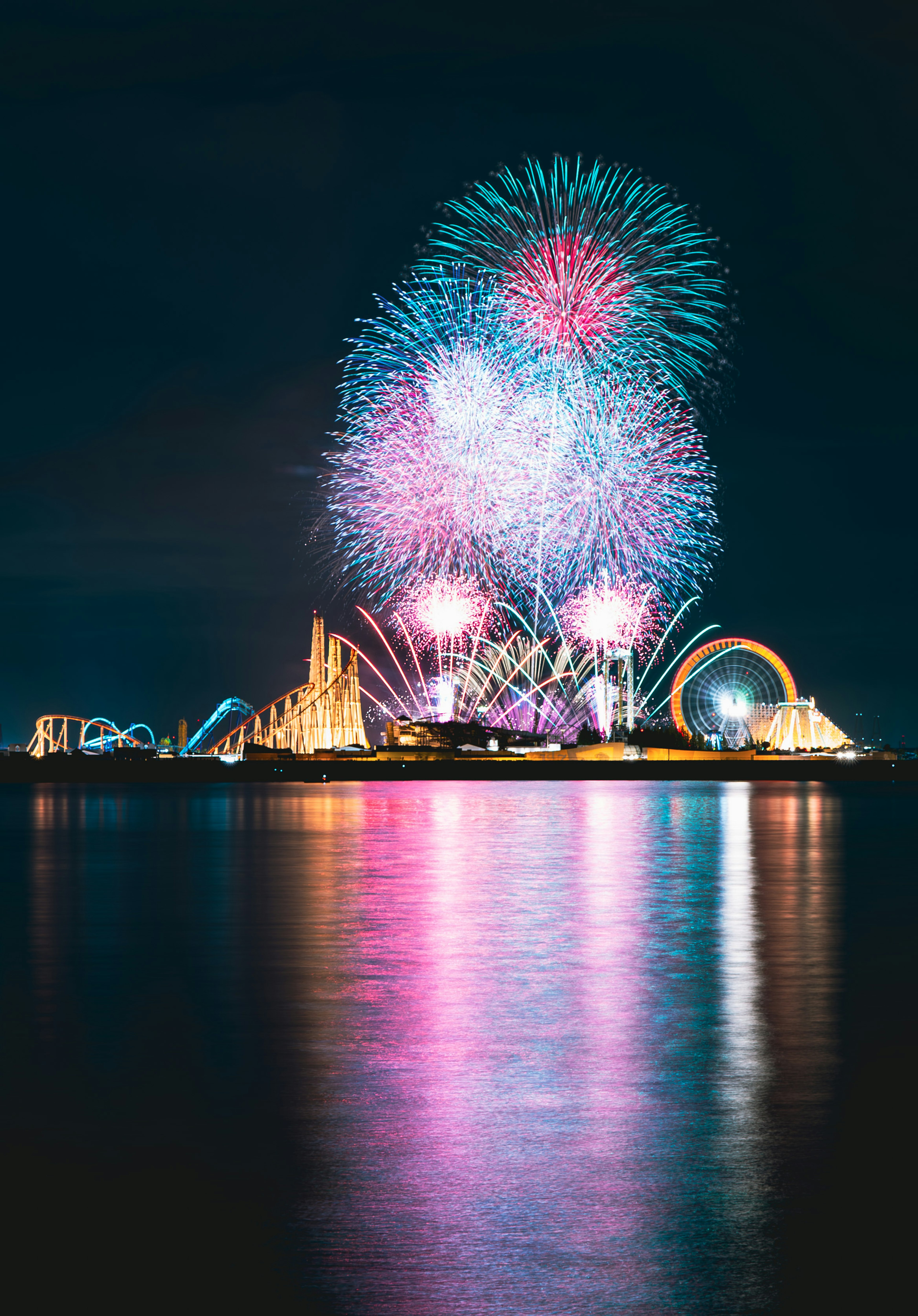 夜空に色とりどりの花火が打ち上げられ遊園地のアトラクションが映える風景