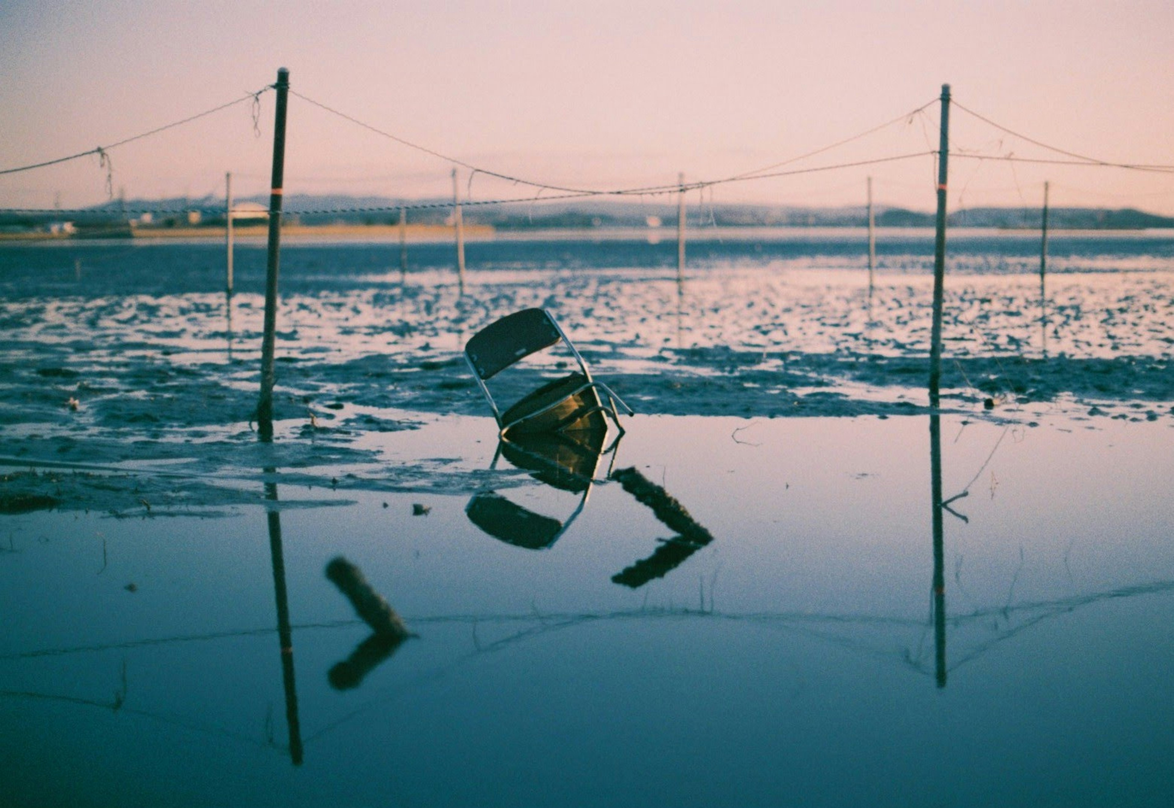 Ein teilweise im Wasser stehender Stuhl mit Reflexionen und Pfosten im Hintergrund