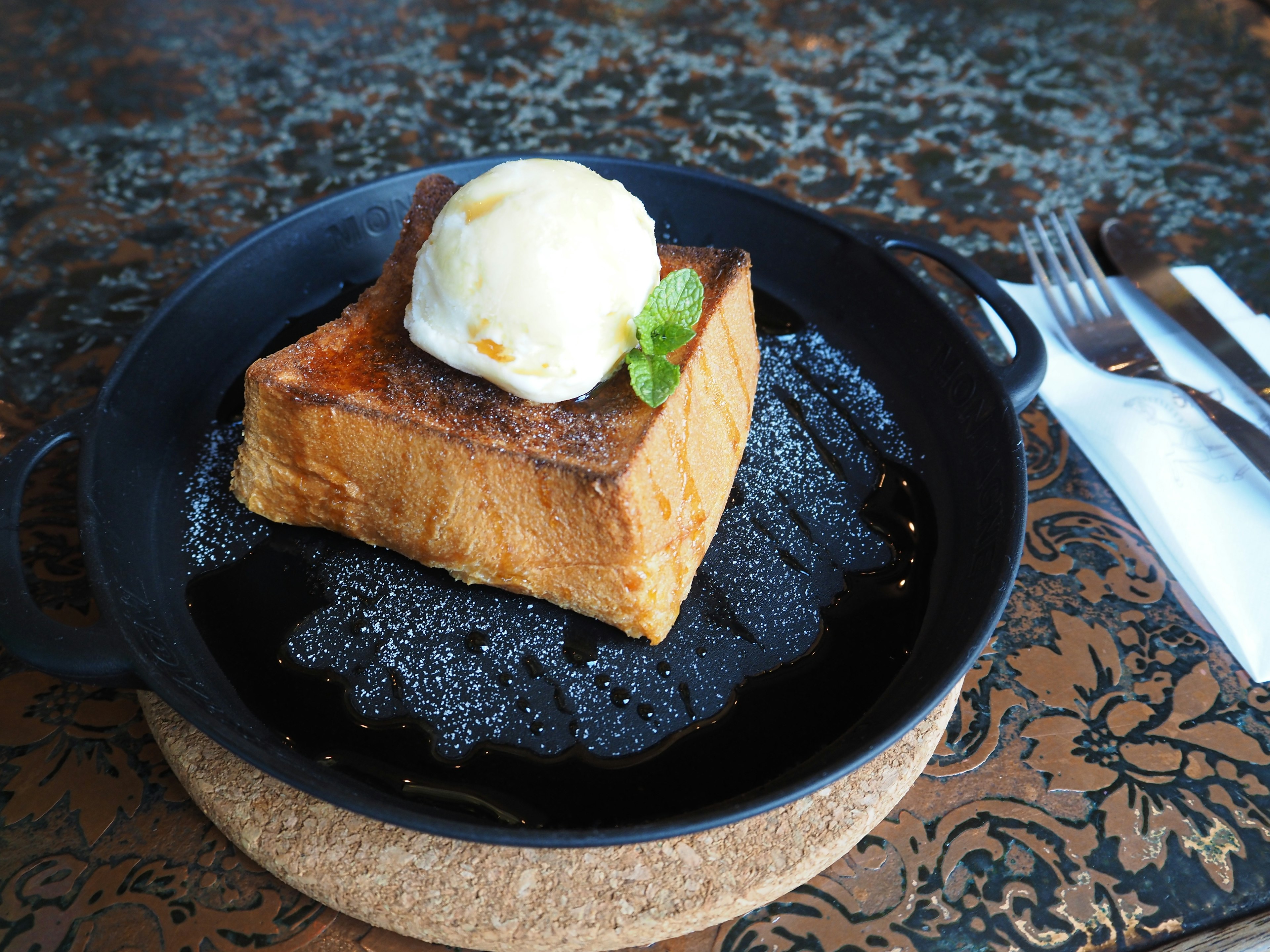 Toasted bread pudding topped with vanilla ice cream served on a black plate