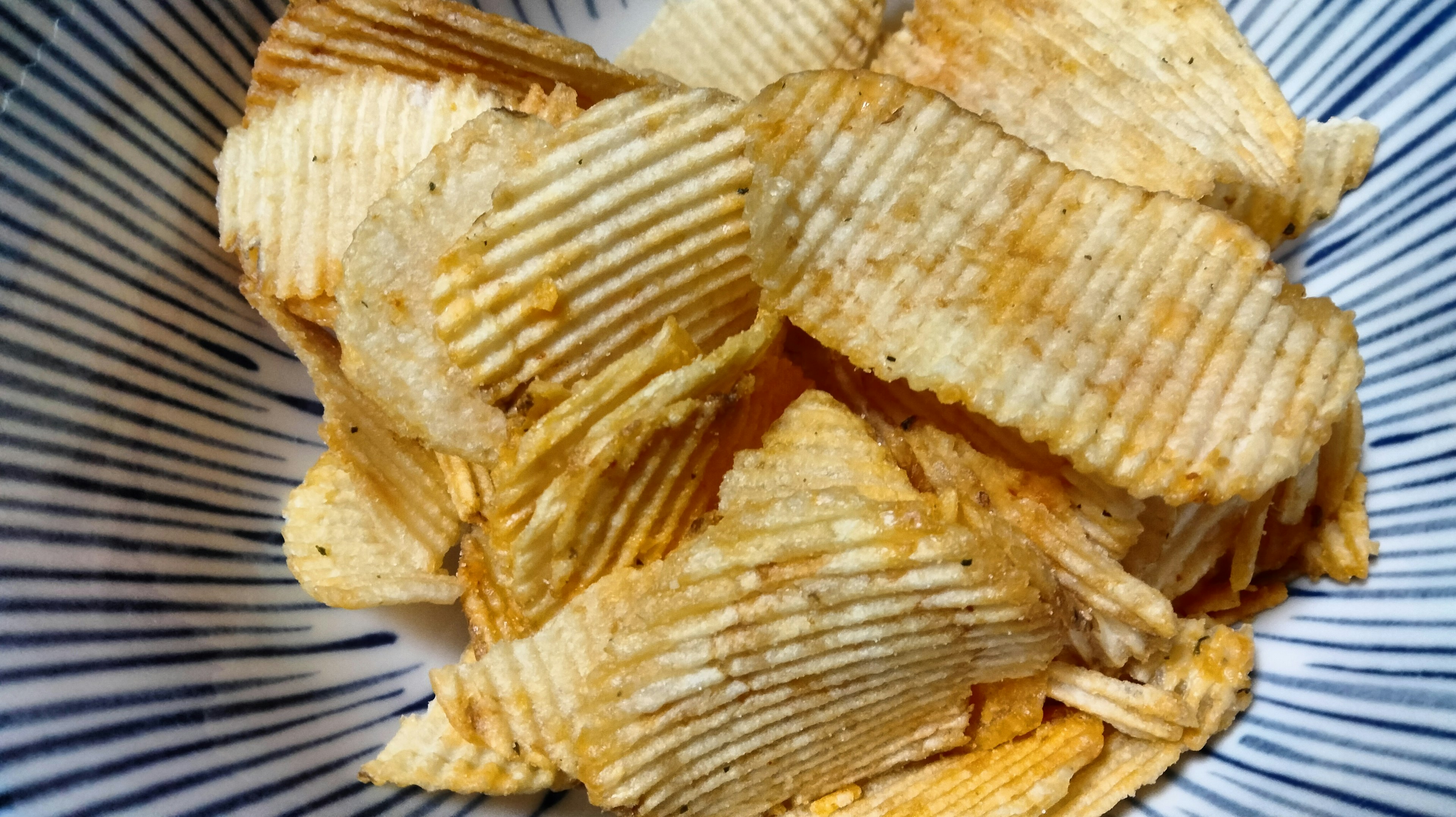 Wavy potato chips arranged in a blue striped bowl