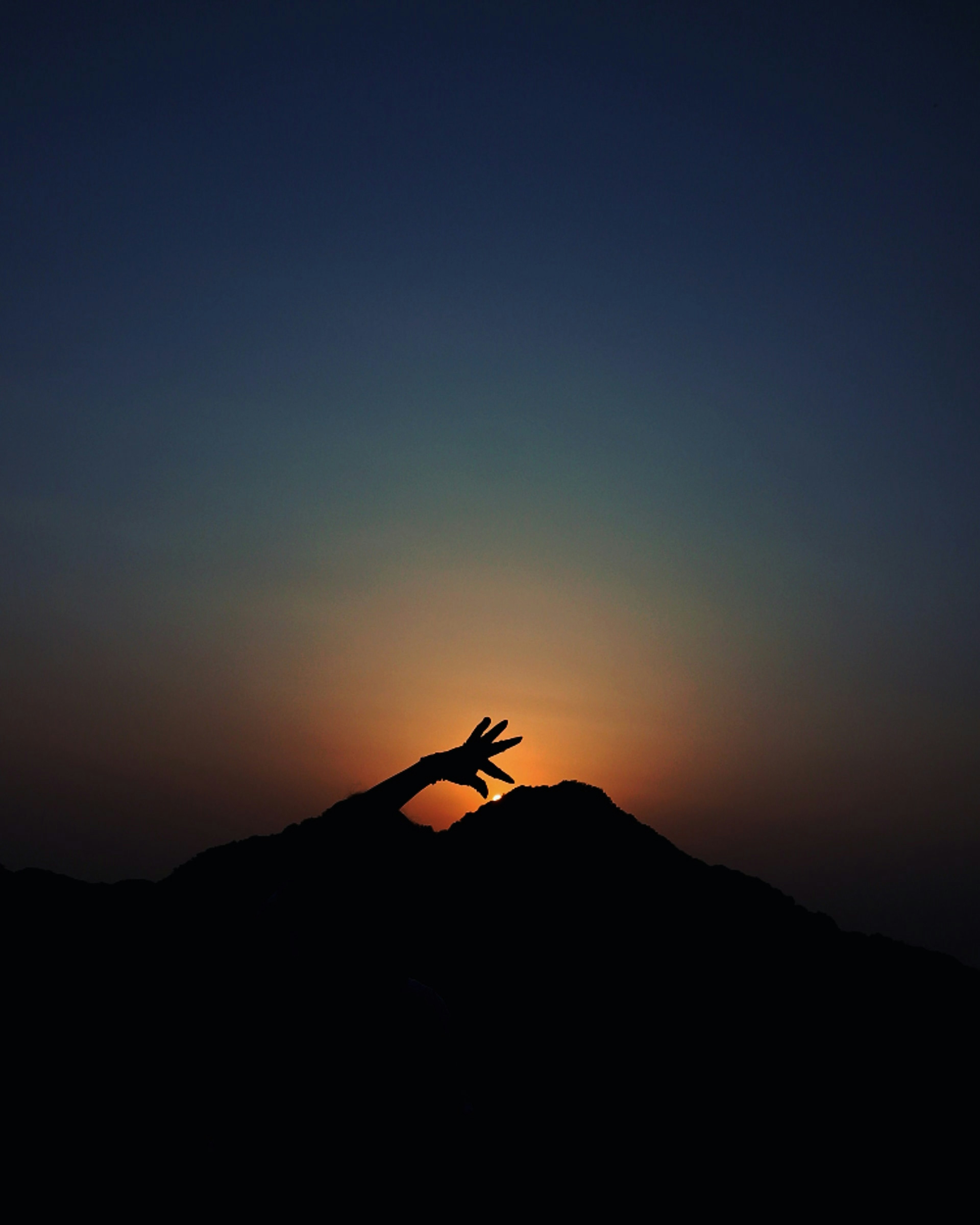 Silhouette di una mano che raggiunge il sole dietro una montagna