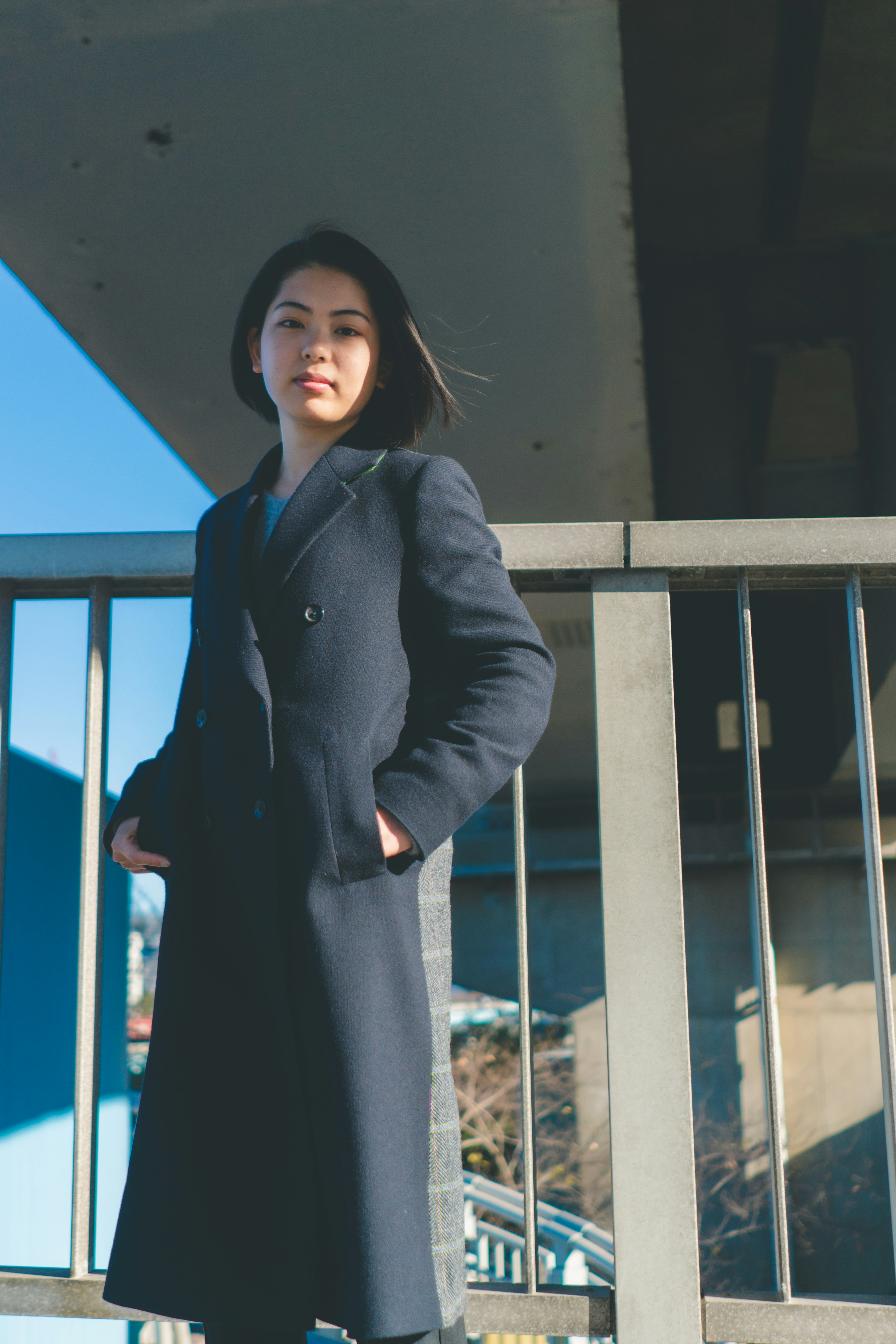 A woman in a black coat standing under a bridge with a blue sky