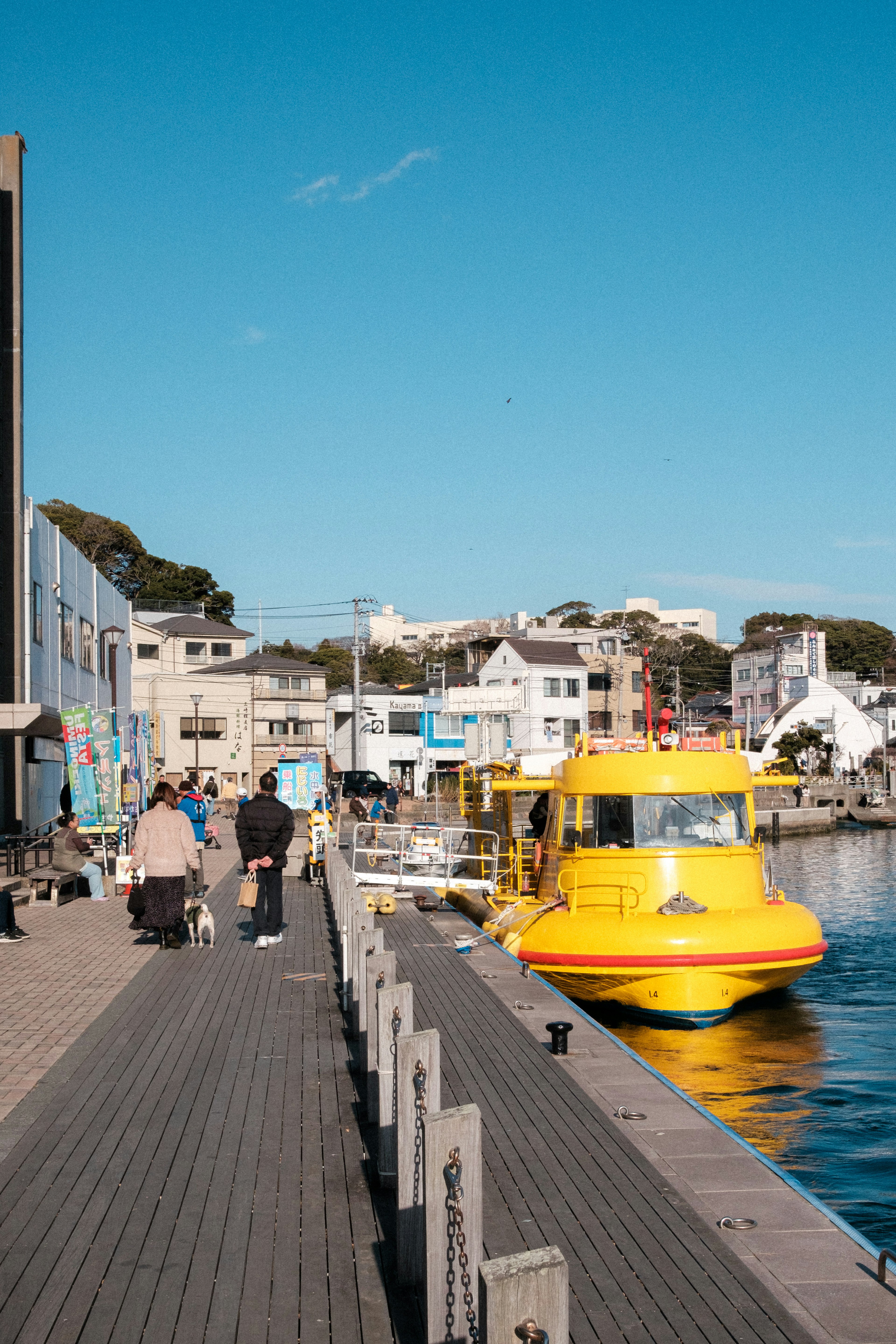 A bright yellow boat docked at the waterfront with people strolling nearby