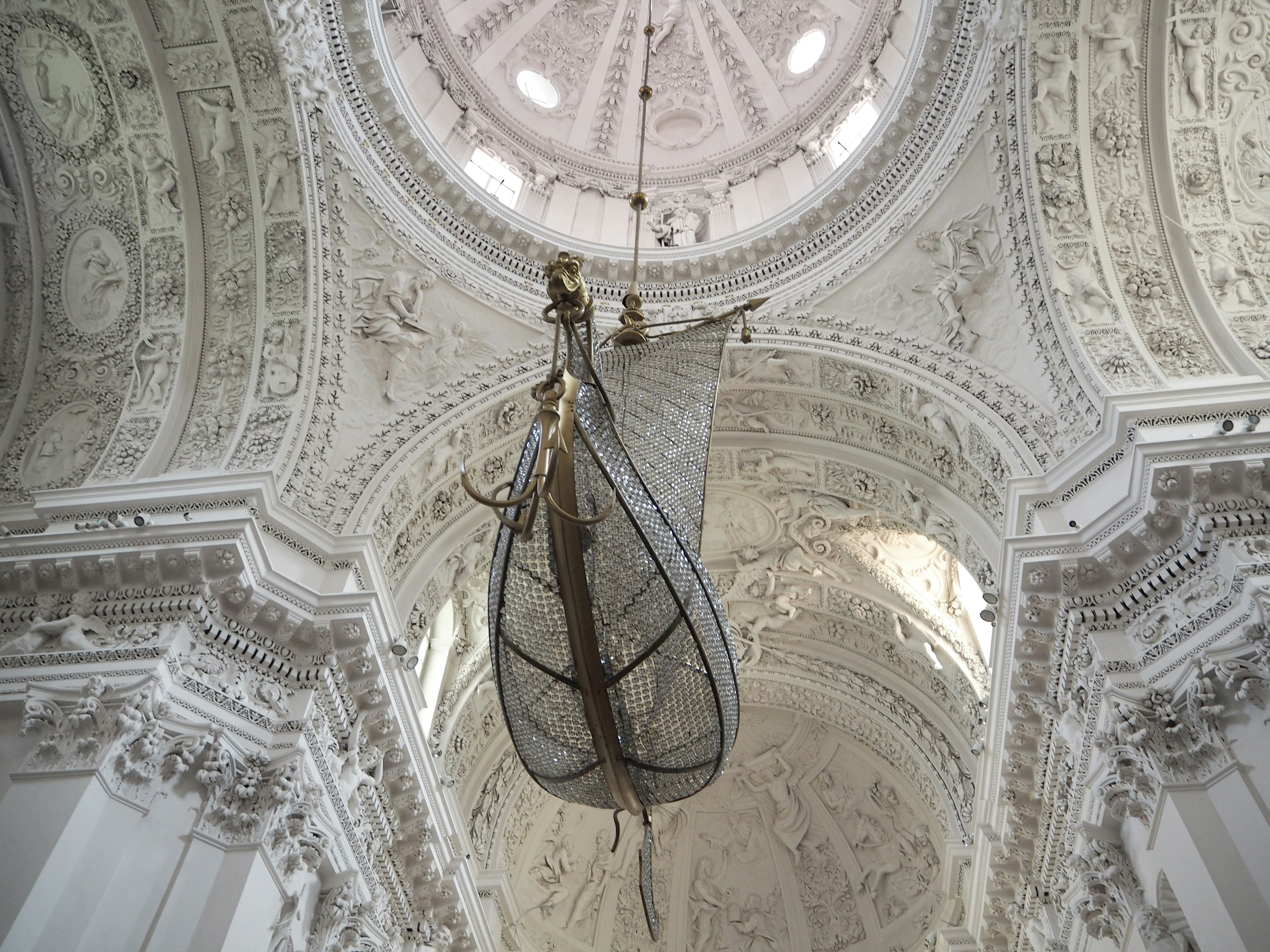 A stunning chandelier shaped like a boat suspended beneath a beautifully decorated white ceiling