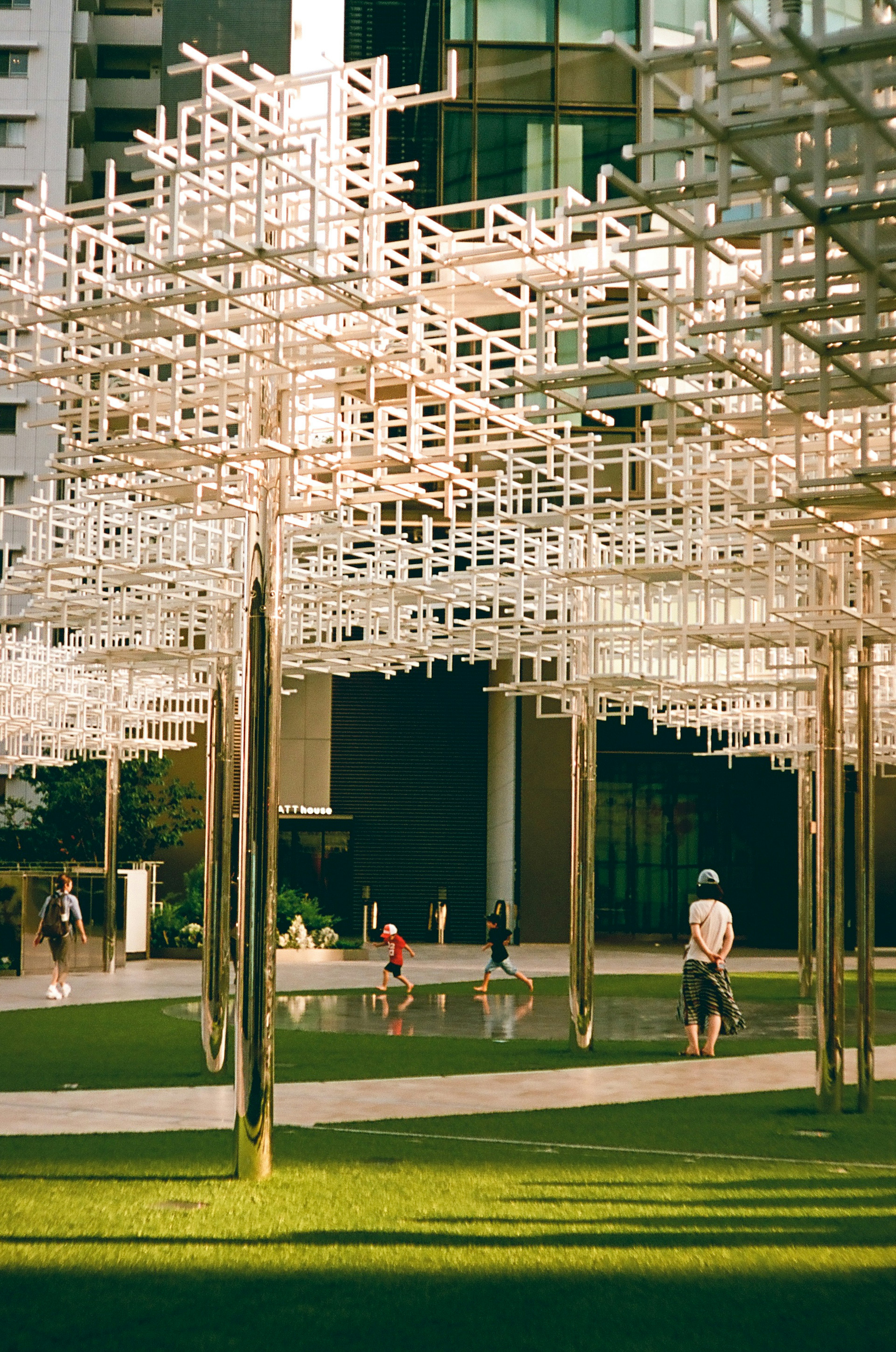 People playing under a white structured installation in front of a modern building