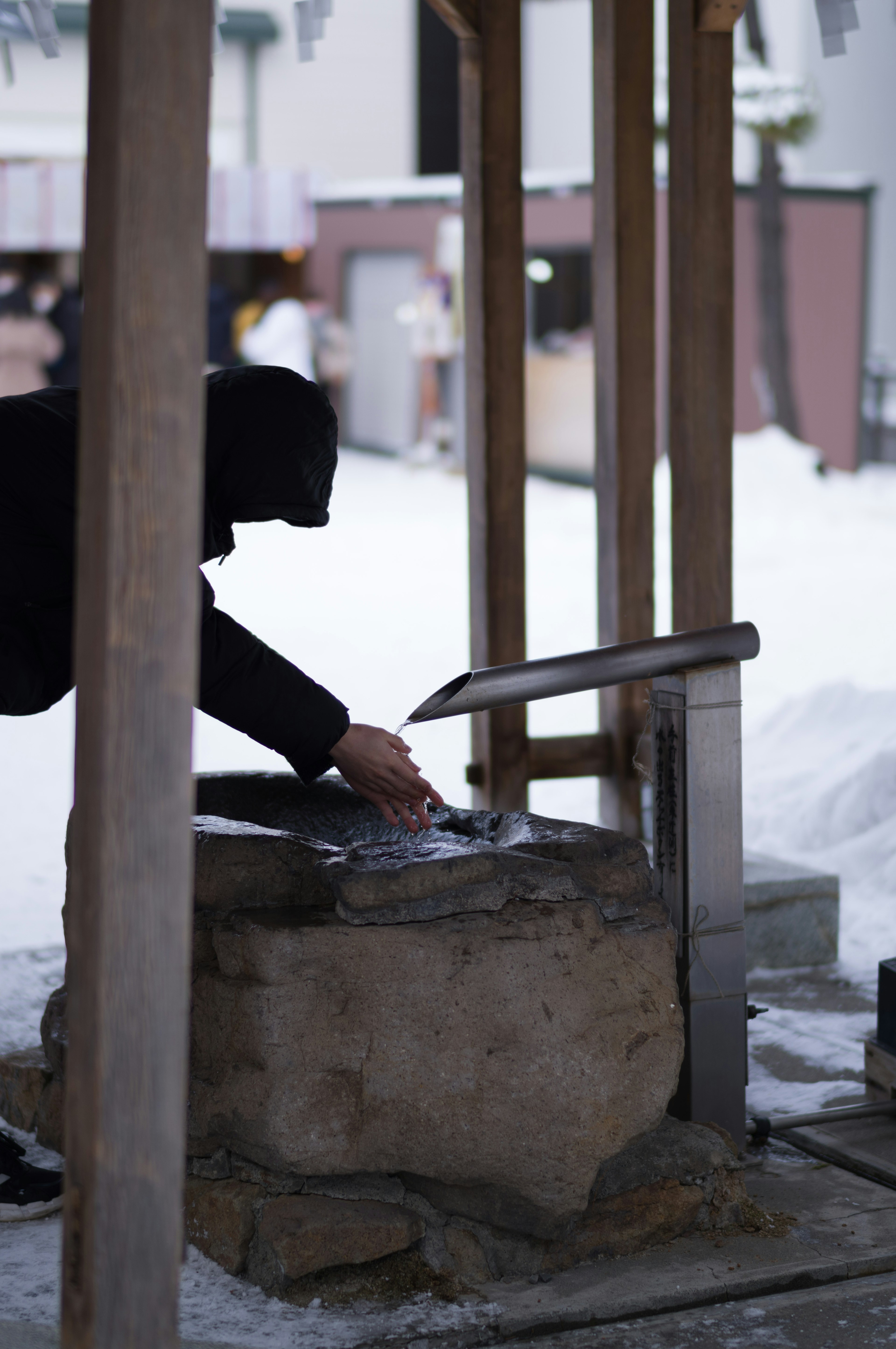 雪の中で手を洗う人の姿と石の洗い場