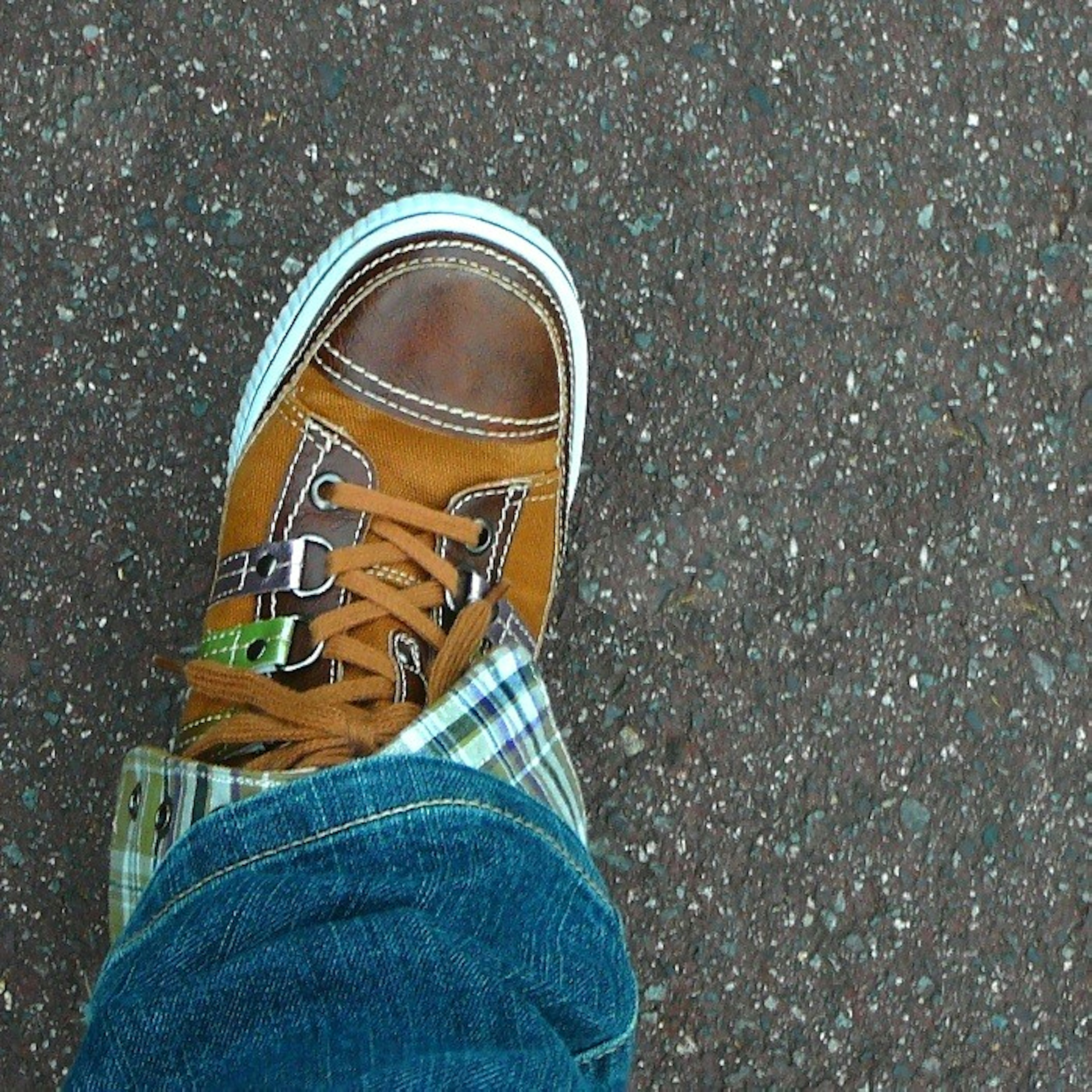 Vue rapprochée d'une chaussure de sport marron et d'un jean bleu sur une surface texturée