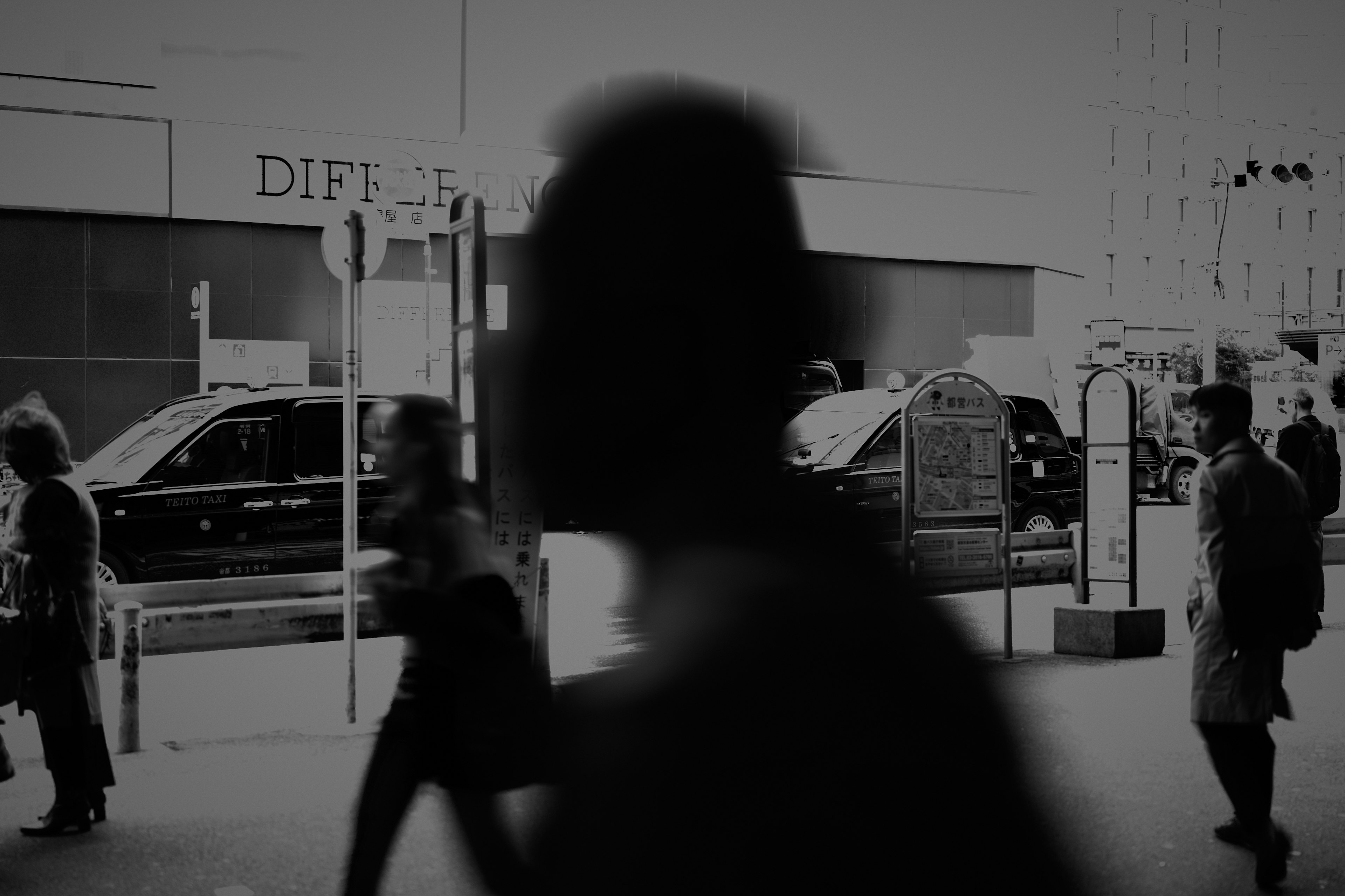 Black and white scene of people walking on the street with buildings and cars in the background