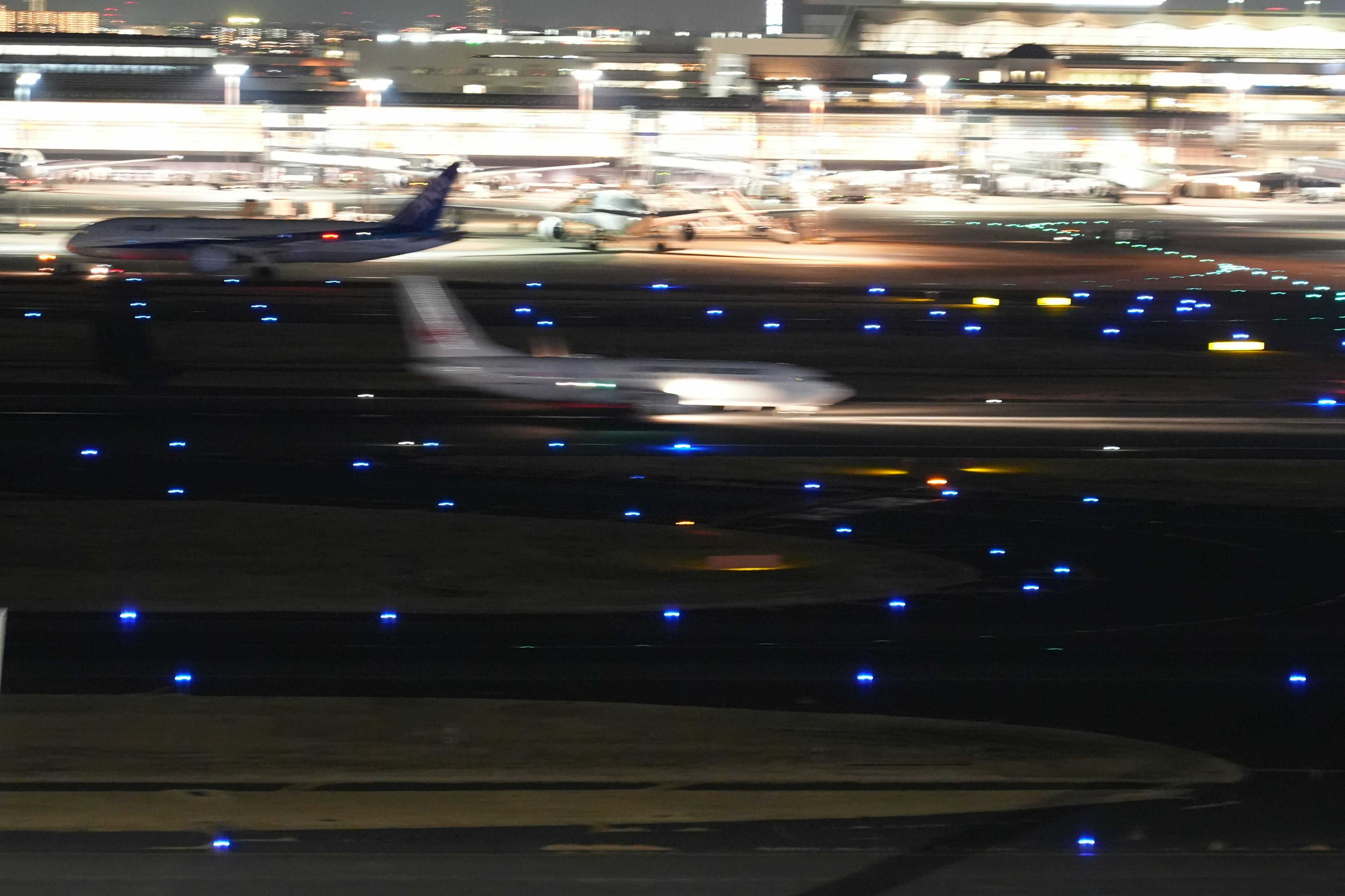 A plane taxiing on a runway at night illuminated by blue lights