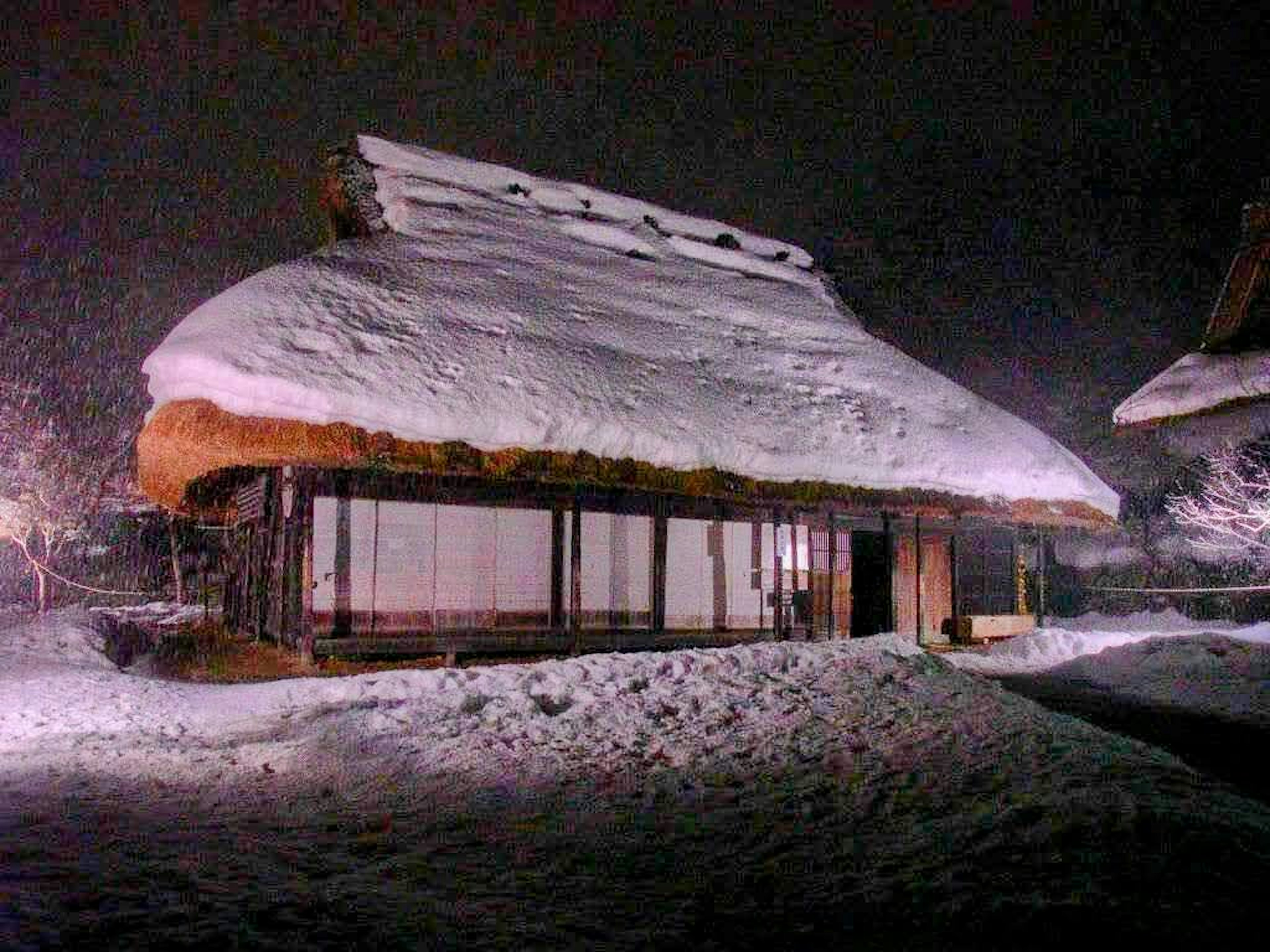 Rumah tradisional Jepang yang tertutup salju diterangi di malam hari