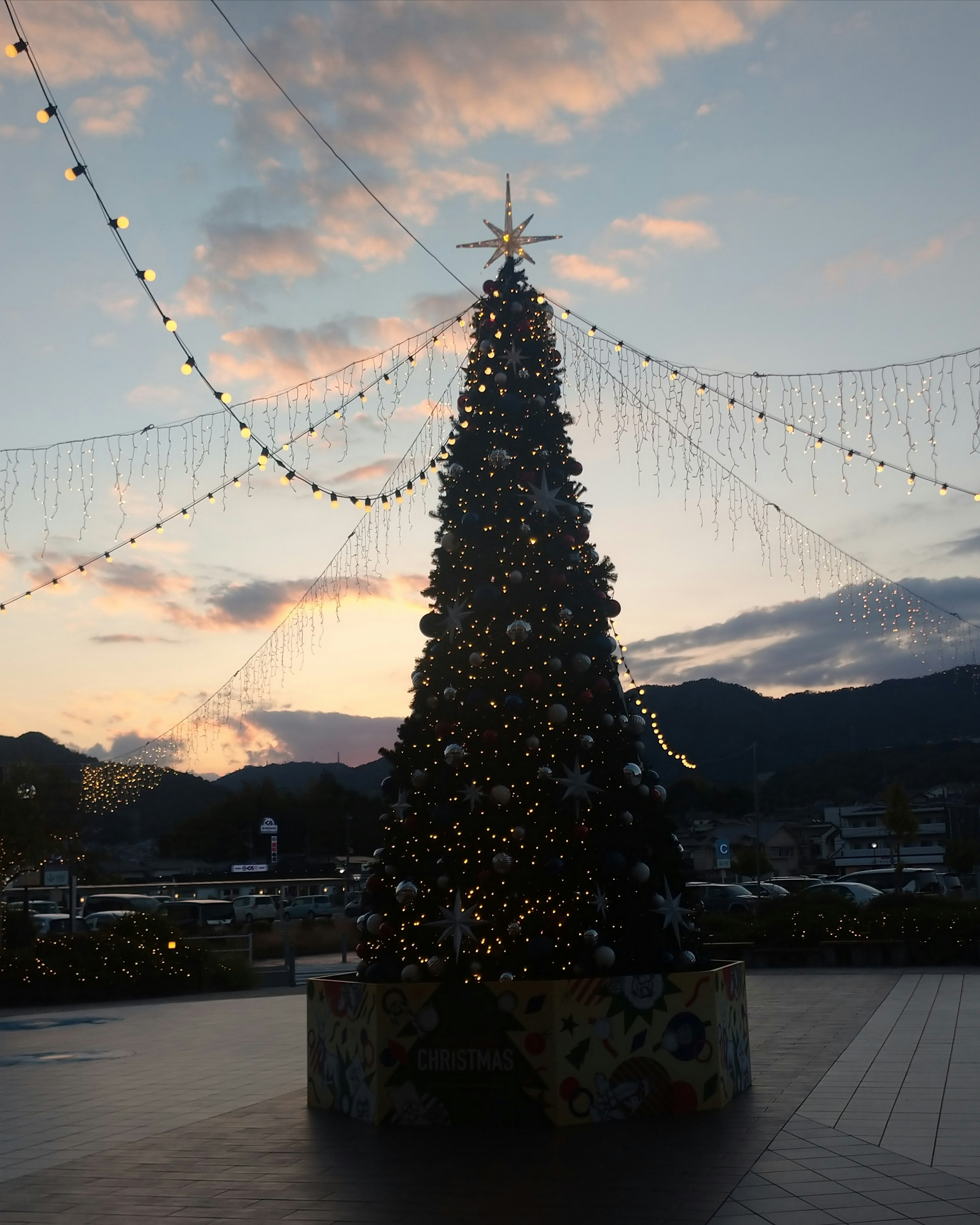 Christmas tree adorned with lights under a sunset sky