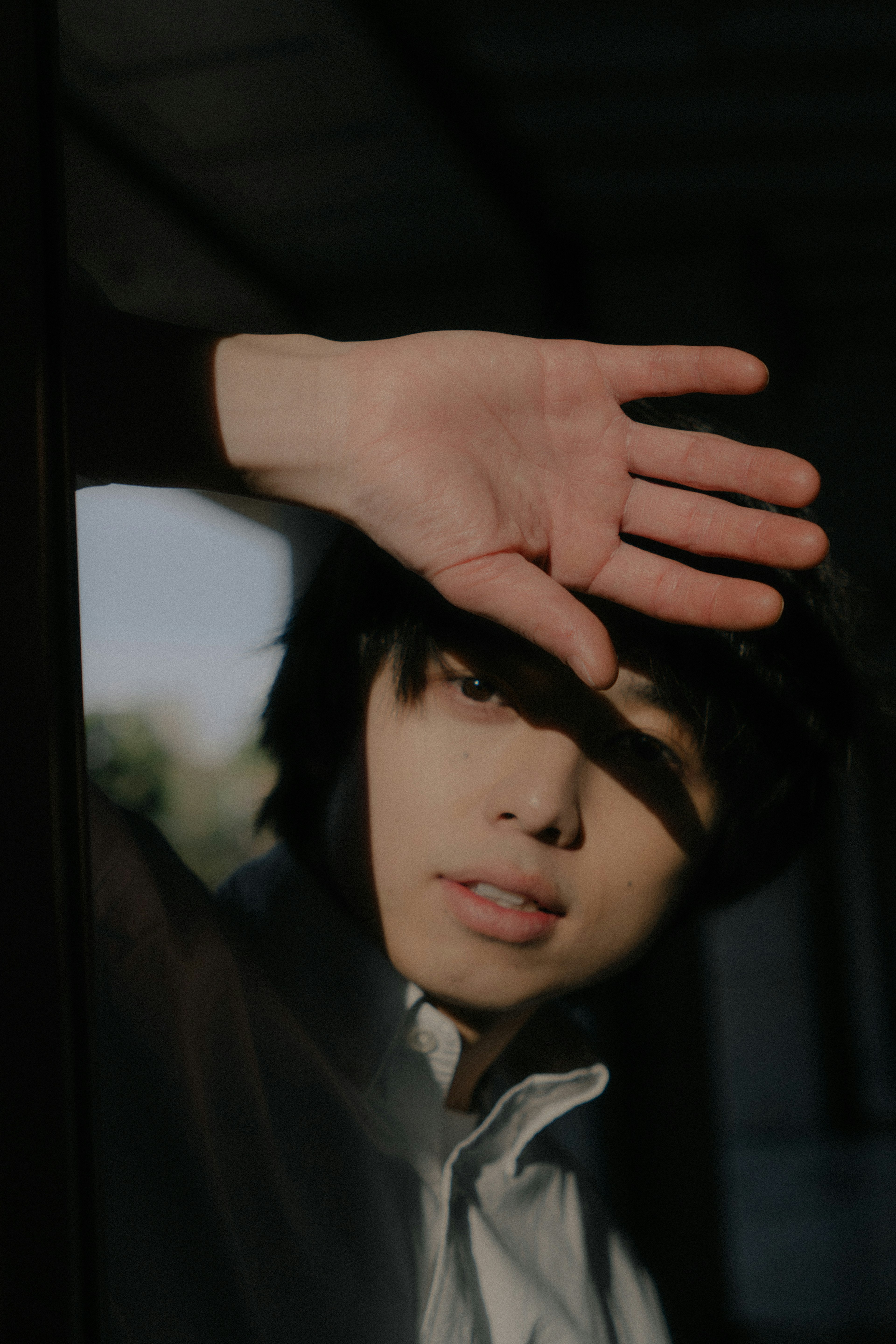 Young man standing by a window shielding his eyes from sunlight