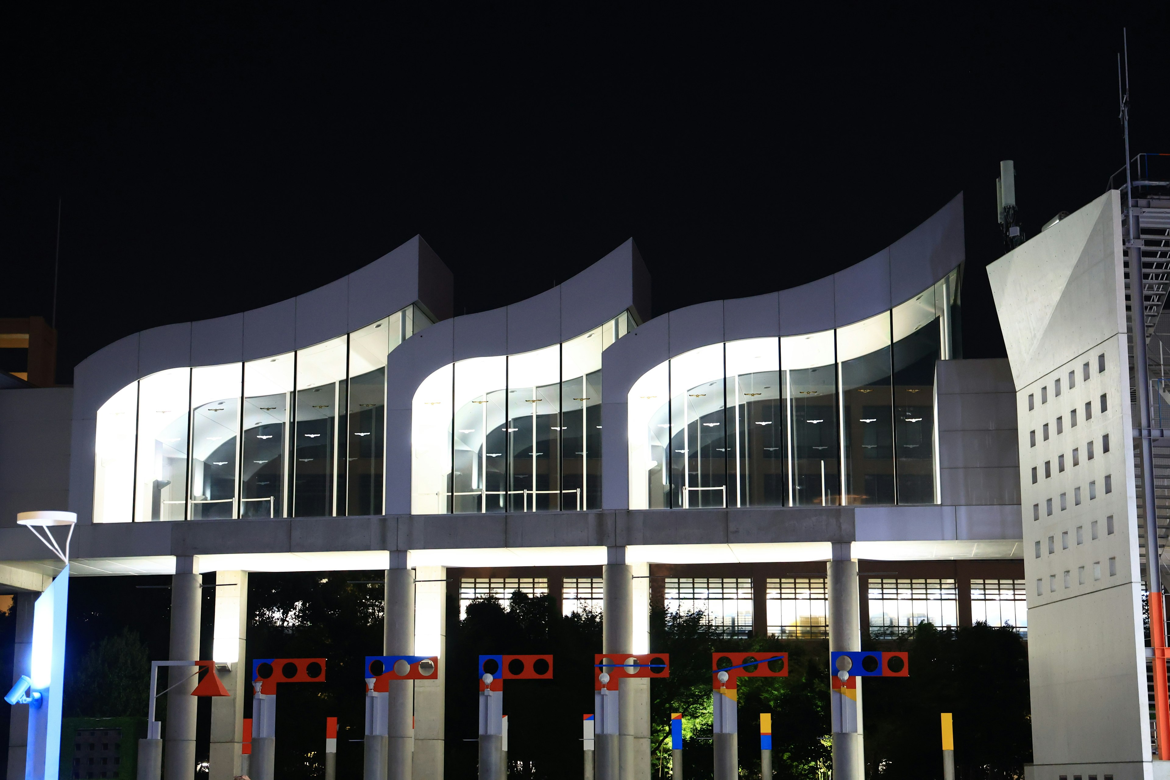 Façade d'un bâtiment moderne avec trois toits en forme de vague éclairés la nuit